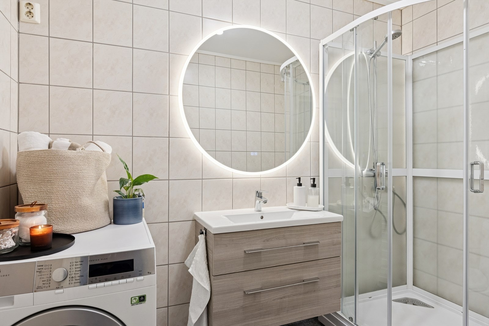 Badet er delikat med flislagte vegger i en beige fargenyanse - lys i speil - opplegg for vaskemaskin Galleribilde
