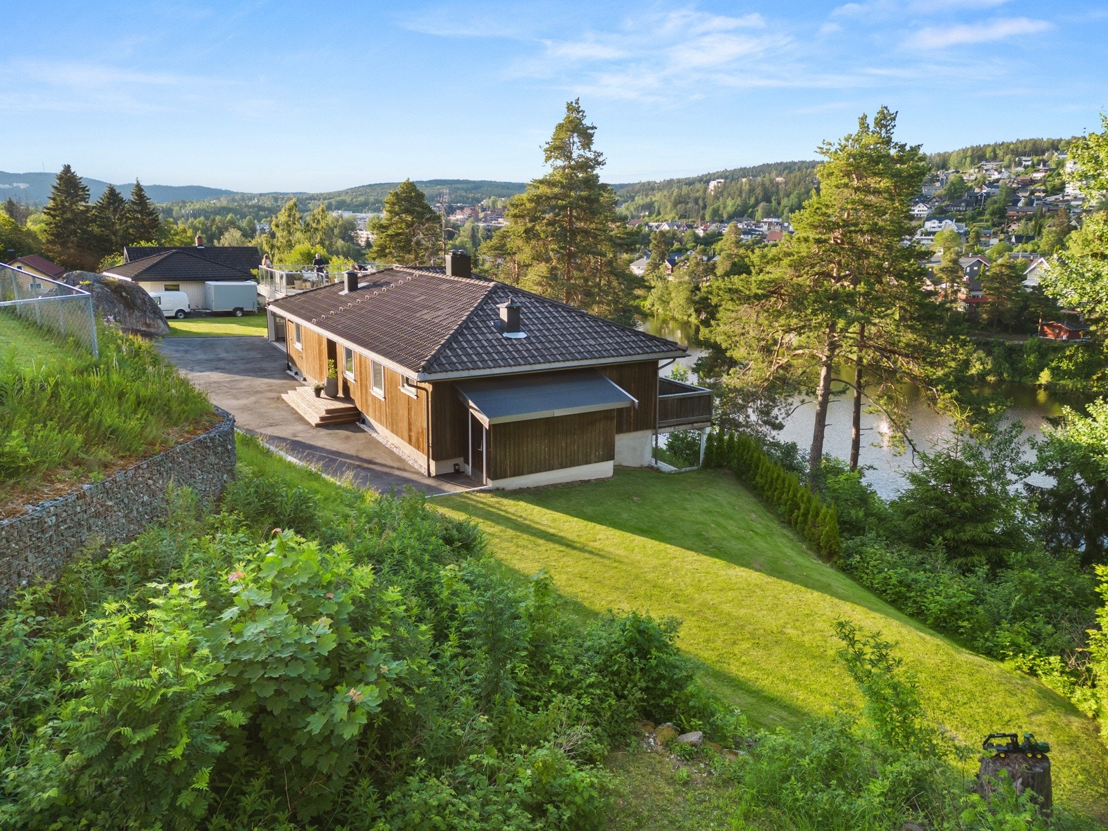 Tomten skrår ned mot Langvannet, og den velstelte hagen rammes inn med frodig, grønn vegetasjon. Galleribilde