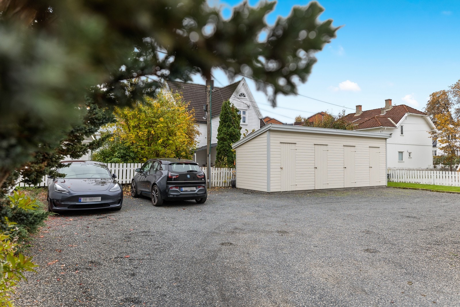 Gruset gårdsplass med parkering og utvendig bod Galleribilde