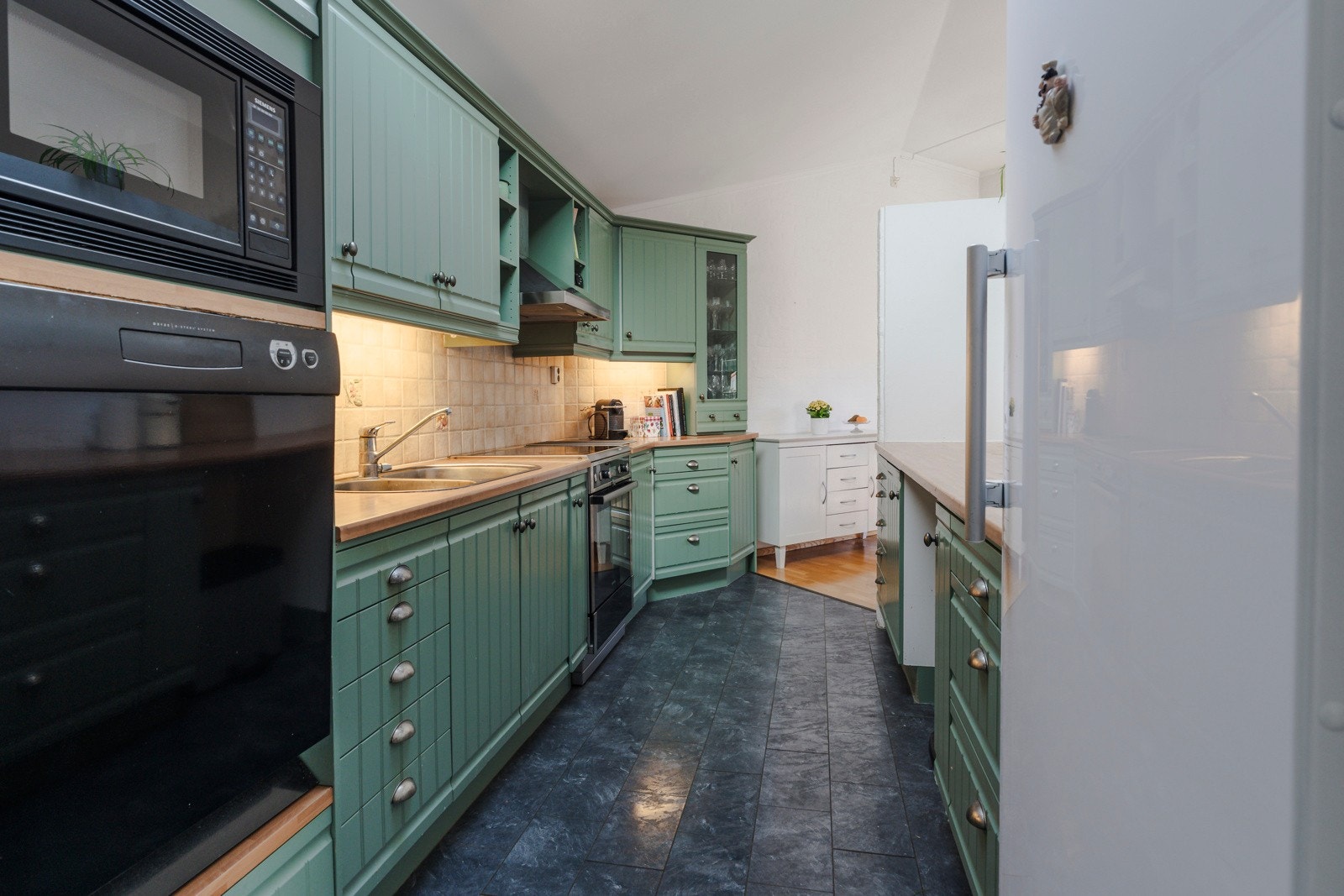 Pent kjøkken med godt av oppbevaring og flere integrerte hvitevarer Galleribilde