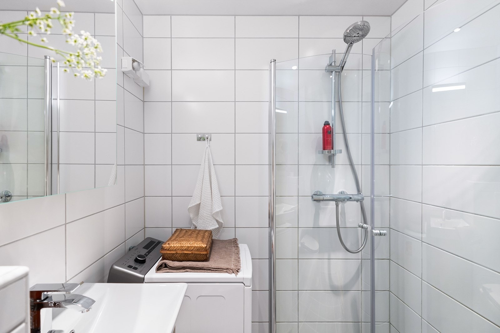 Det er fliser på vegger og gulv, og badet er utstyrt med vegghengt toalett, servant over skuffeseksjon, speilskap og dusjsone Galleribilde