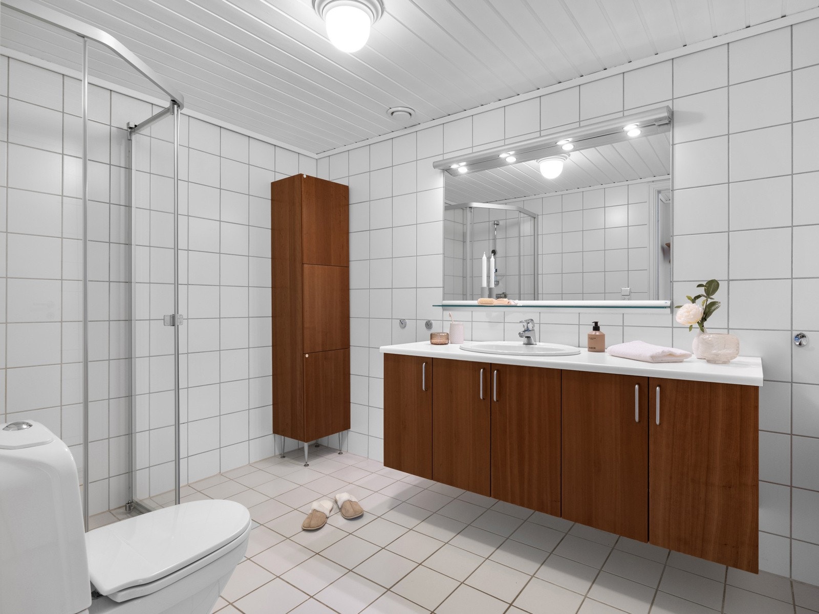 Badet fremstår lyst og innbydende, med helflisede flater i lyse toner som gir et rent uttrykk. Innredningen består av servant med tidsløse fronter, dusjhjørne, toalett og praktisk oppbevaringsskap. Galleribilde