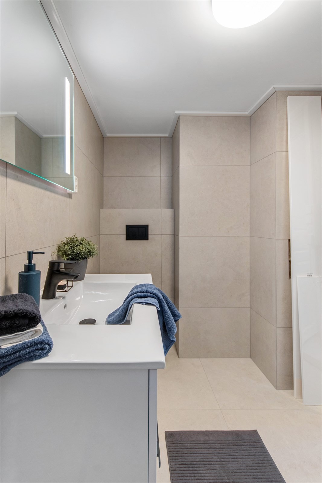Badet har hvit servantinnredning, vegghengt toalett og speil med integrert belysning Galleribilde