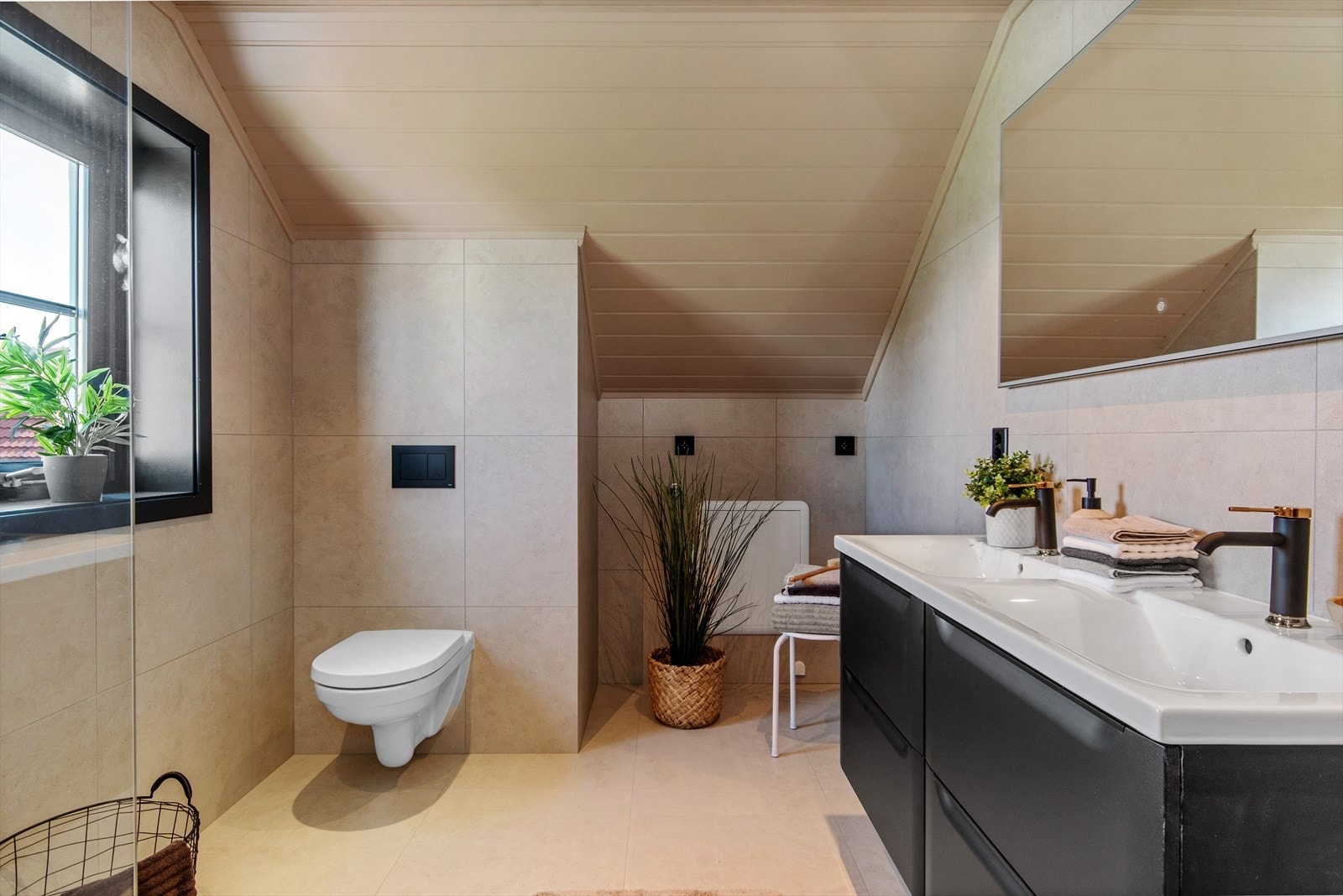 Smakfullt bad med flislagte overflater, varme i gulv og formpresset panel i himling. Badet har en moderne standard med innredning i mørk utførelse, dobbel servant og opplegg for vaskemaskin. Galleribilde