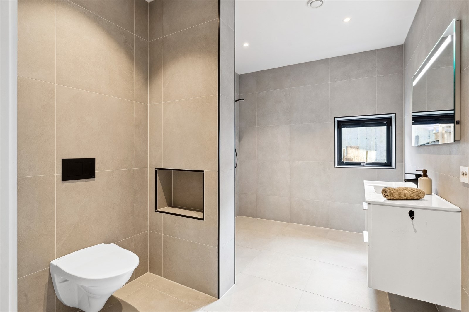 Lyst og moderne bad med stilrene fliser, vegghengt toalett og romslig dusj. Galleribilde