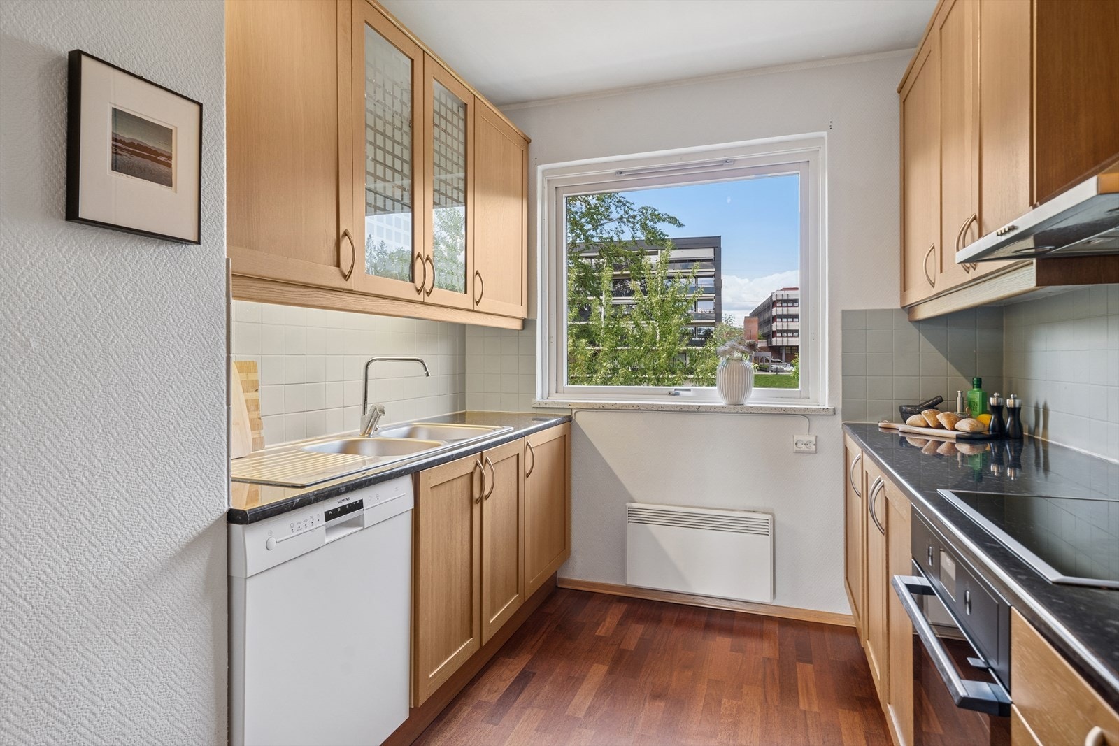 Praktisk kjøkkenløsning med integrert platetopp, stekeovn fra 2025 med pyrolyse og oppvaskmaskin i nisje. Benkeplaten i laminat har nedfelt kum i kompositt og godt med arbeidsflate. Galleribilde