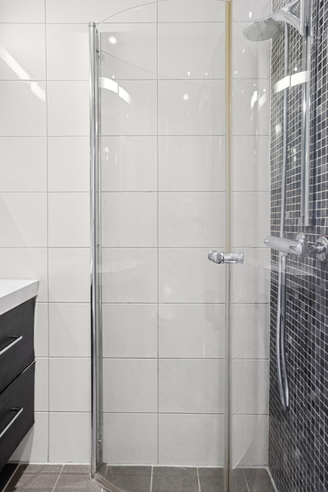 Badet består av innredning med heldekkende servant med speilskap med lys over, veggehengt toalett med skjult sisterne og dusjhjørne med innfellbare glassdører. Galleribilde