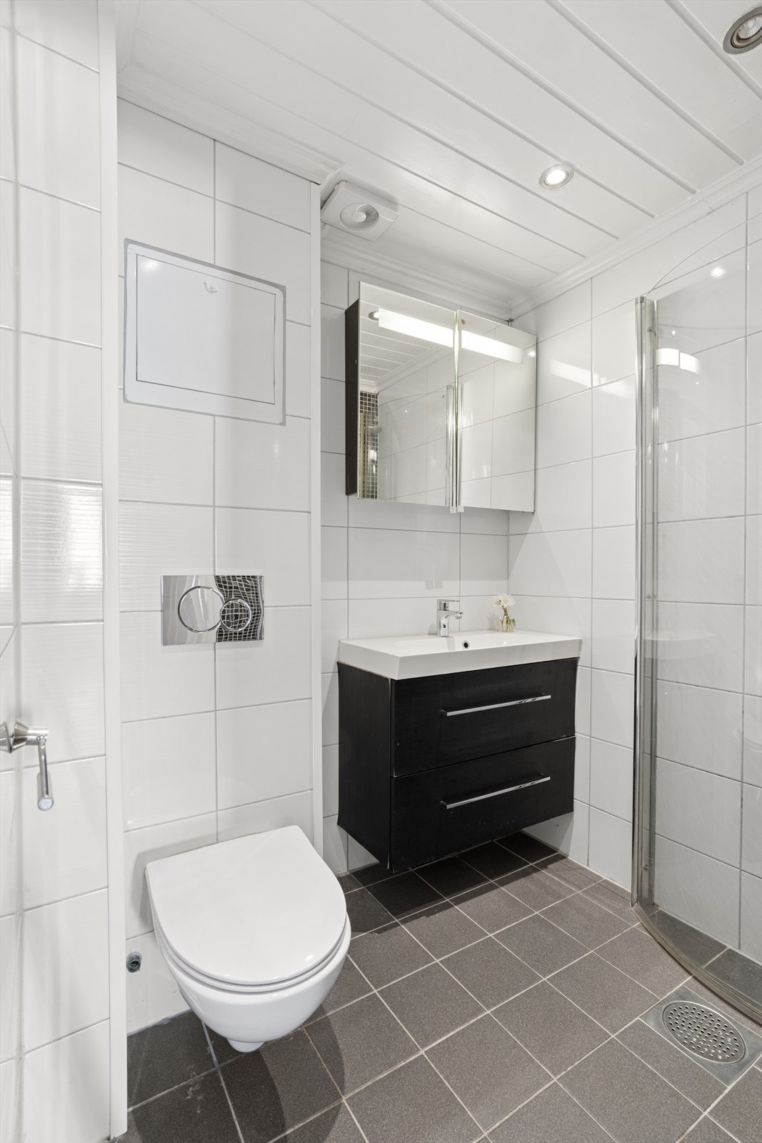 Flislagt bad med gulvvarme med en tidløs standard. Det er hvite fliser på veggene og grå fliser på gulvet. Galleribilde