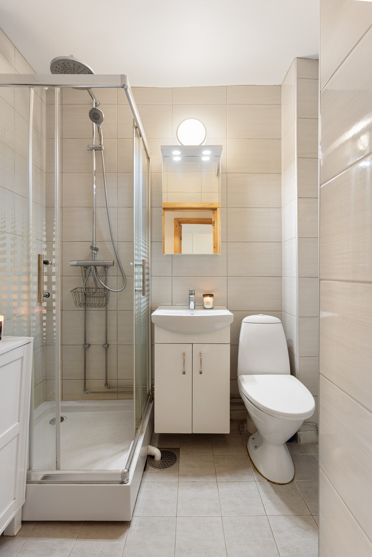 Badet har flislagte vegger og gulv, og fasilitetene består av servant med slette fronter, gulvstående toalett, dusjkabinett og opplegg for vaskemaskin Galleribilde