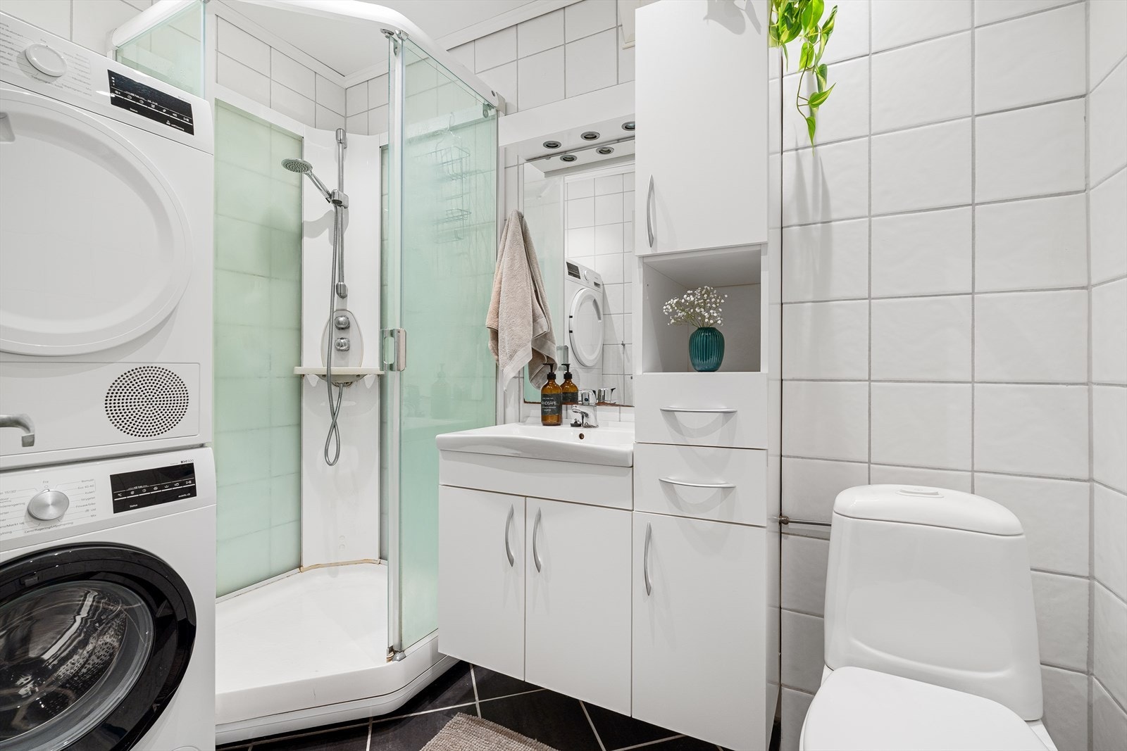 Badet er helfliset med varme i gulvet og inneholder et praktisk dusjkabinett, baderomsinnredning med speil og belysning over, toalett, samt plass og opplegg for vaskemaskin/tørketrommel. Galleribilde