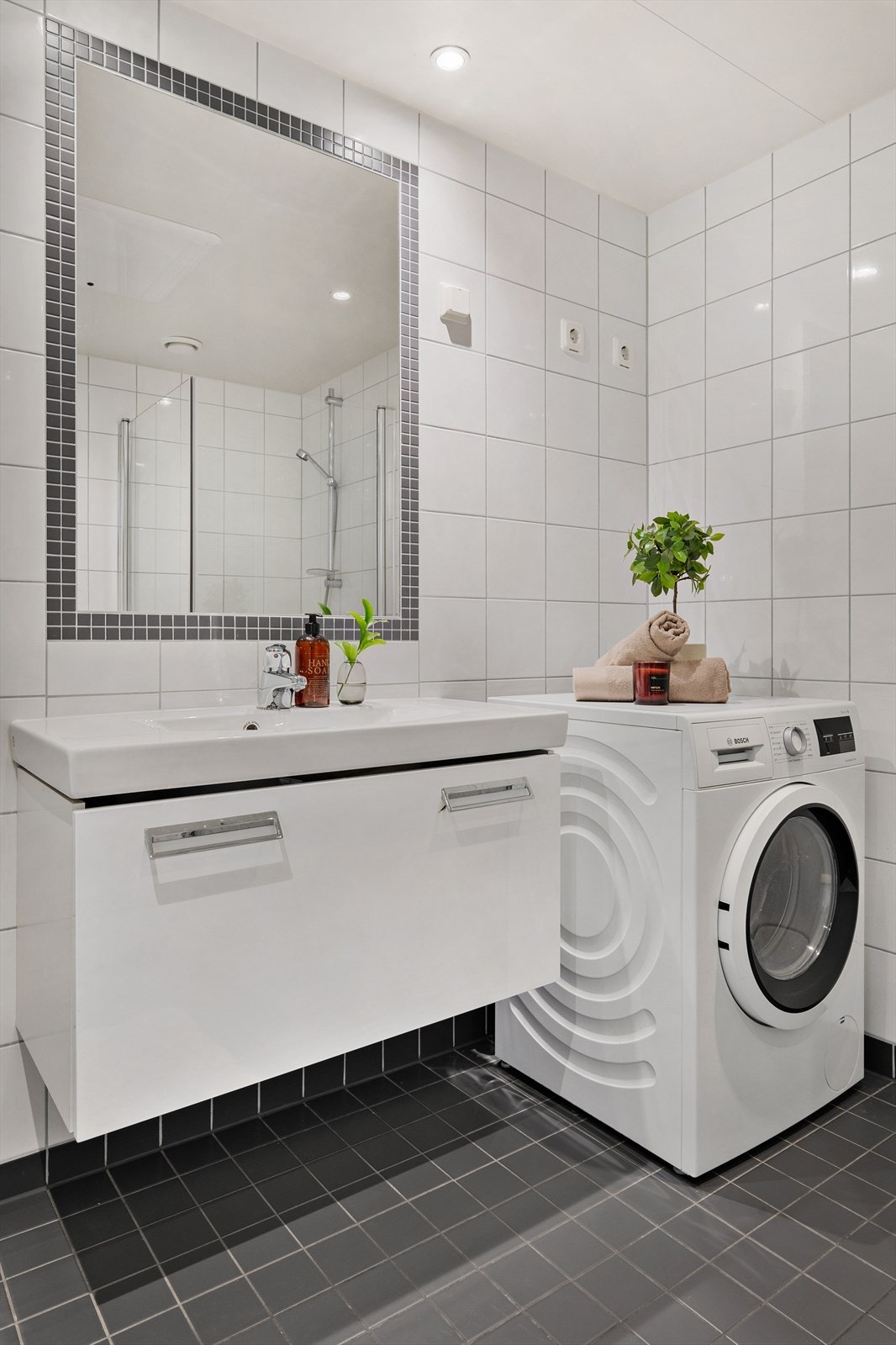 Bad har en fin størrelse og består av servant med underskap, innmurt speil, dusjhjørne, veggmontert toalett med innebygget sisterne, dimbare downlights, og opplegg for vaskemaskin Galleribilde