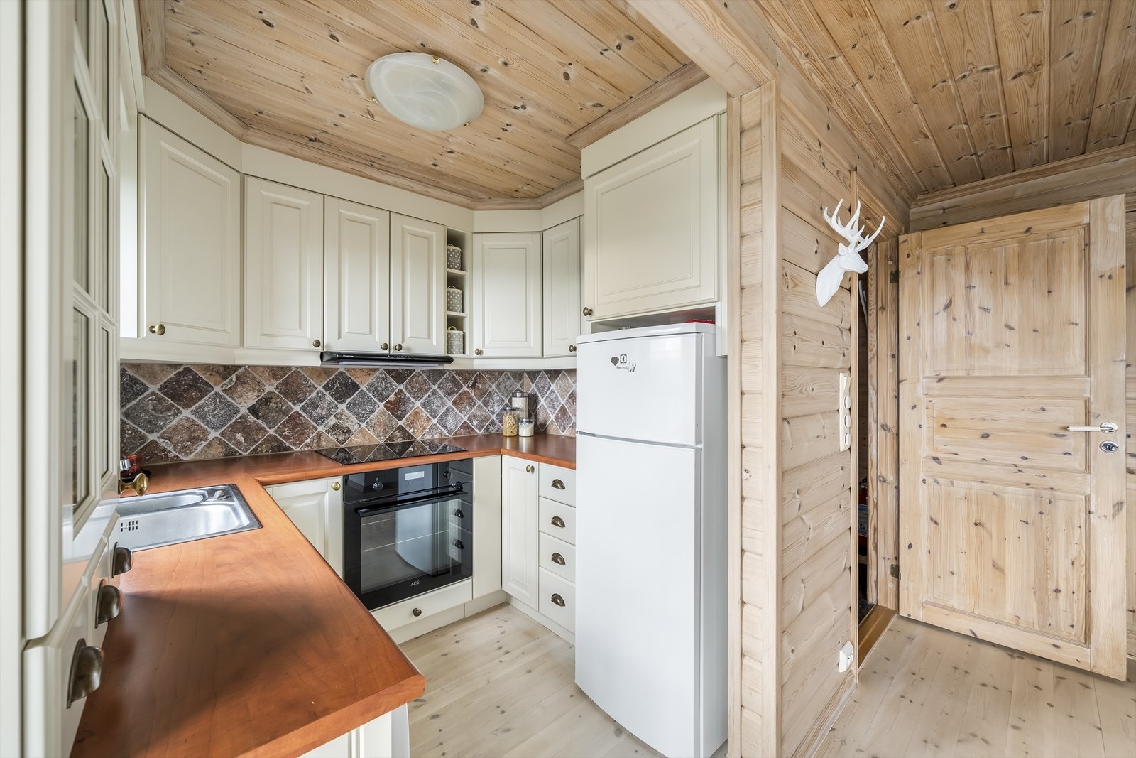 Koselig Hamran-kjøkken med profilerte fronter og fliser mellom over- og underskap. God skap- og benkeplass, samt innebygde og frittstående hvitevarer som medfølger. Galleribilde