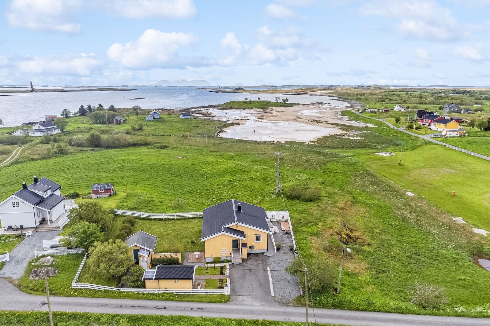 Nydelig utsikt sørover mot Vega. Det er etablert støttemurer og steinbelagte stier til bodene i hagen. Inngangspartiet er overbygd og innglasset mot vest. Galleribilde