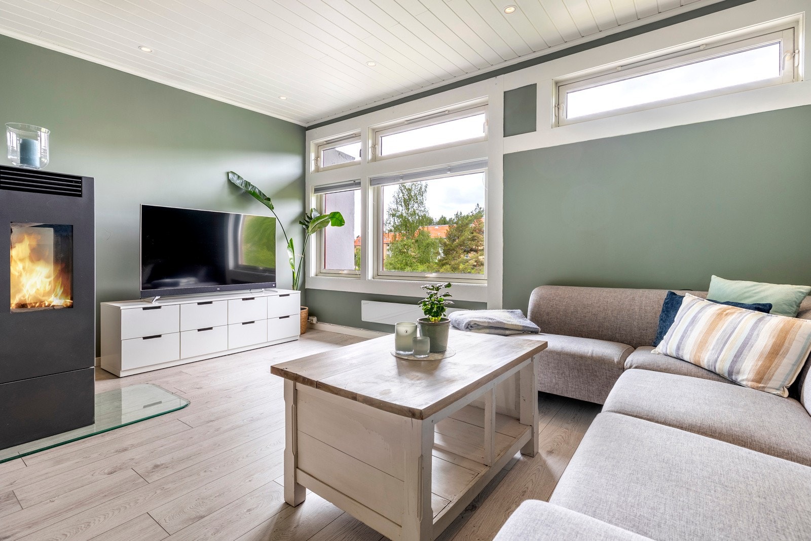 Stuen får rikelig med dagslys og grønt utsyn fra gode, vestvendte vindusflater. Stuen er holdt i samme farger og materialer som kjøkkenet - antikkgrønne vegger, hvitmalt panelhimling med downlights og enstavs laminatgulv, noe som gir en fin helhet. Galleribilde