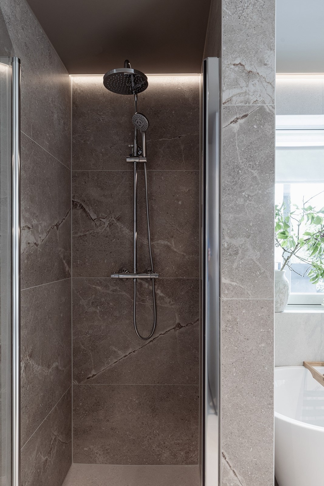 Badet er utformet med storformatflis med sømløse, flislagte benkeplater og dusjnisjer belyst med LED. Flis med tidsriktig utrykk og lett marmorering. Galleribilde