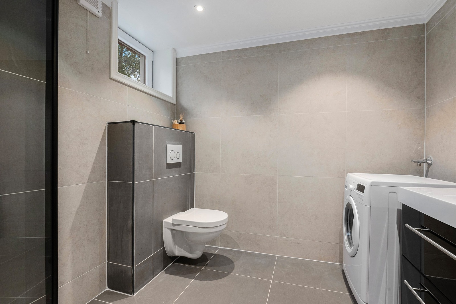 Moderne baderom fra 2025. Flislagt gulv med gulvvarme og flislagte vegger. Nedsenket himling med downlights og malt flate. Vegghengt servantinnredning
med skuffer og ovenpåliggende servant med ett-greps armatur. Speil med lys på vegg over servant. Galleribilde