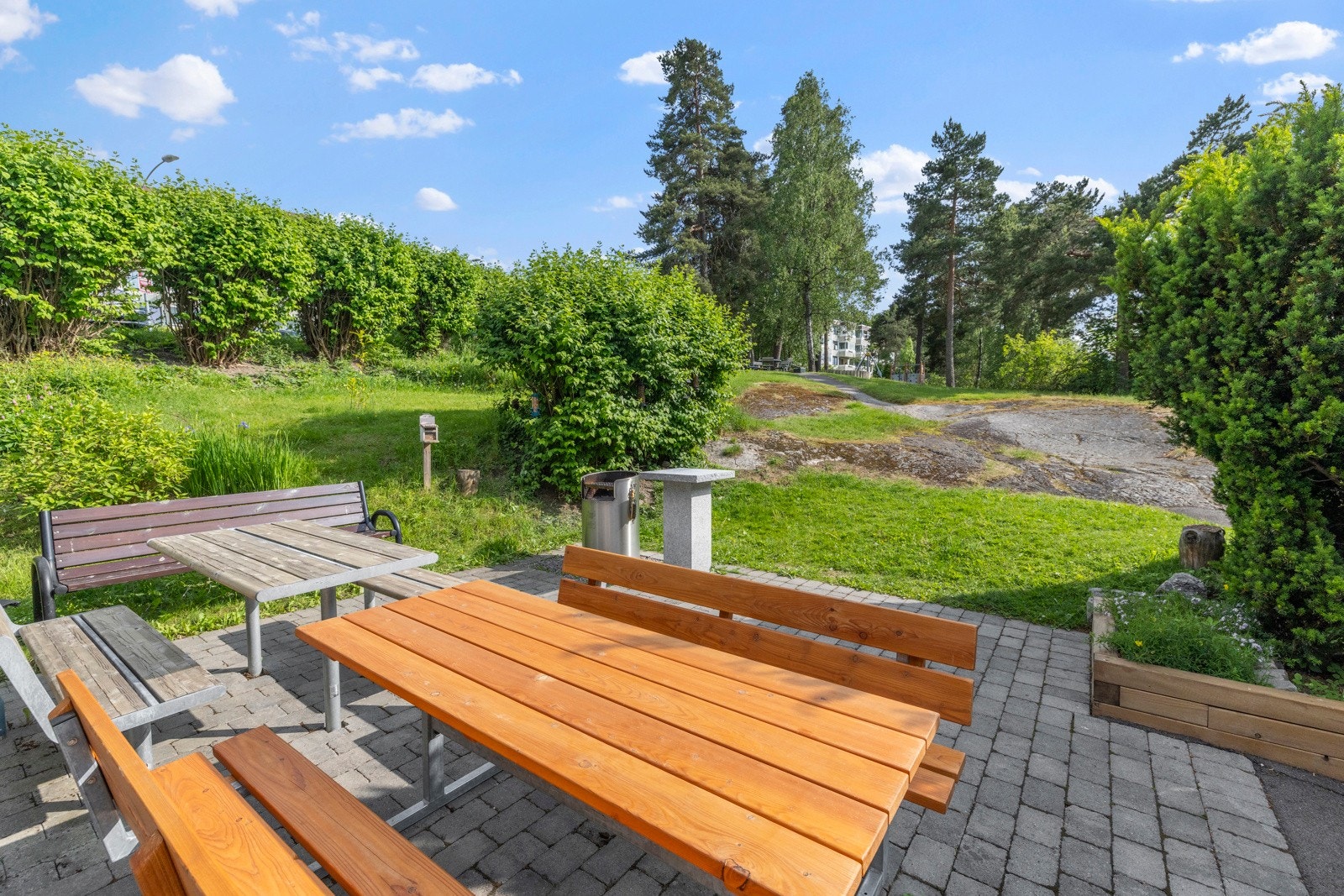 Uteområde med sittebenker og bord, omgitt av grøntområder og trær Galleribilde