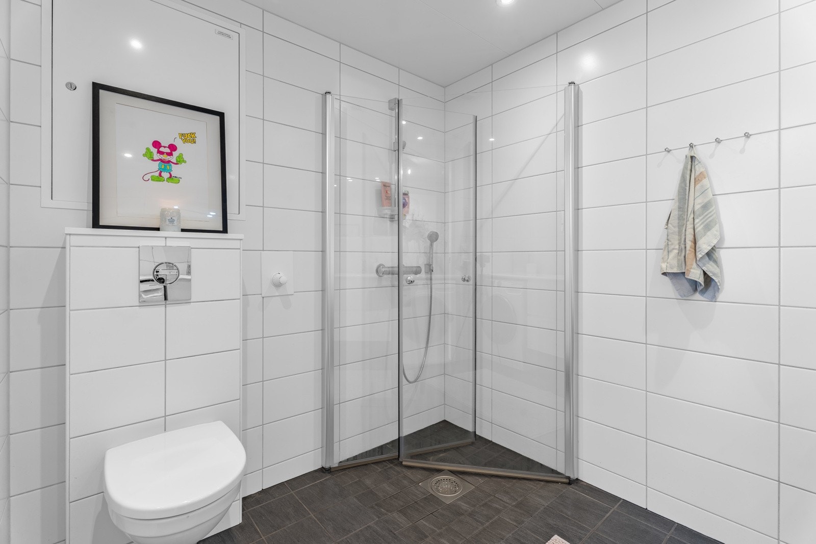 Rommet er innredet med heldekkende benkeplate og servant, underskap, speil med lysarmatur, dusjhjørne, vegghengt toalett og opplegg for vaskemaskin. Galleribilde