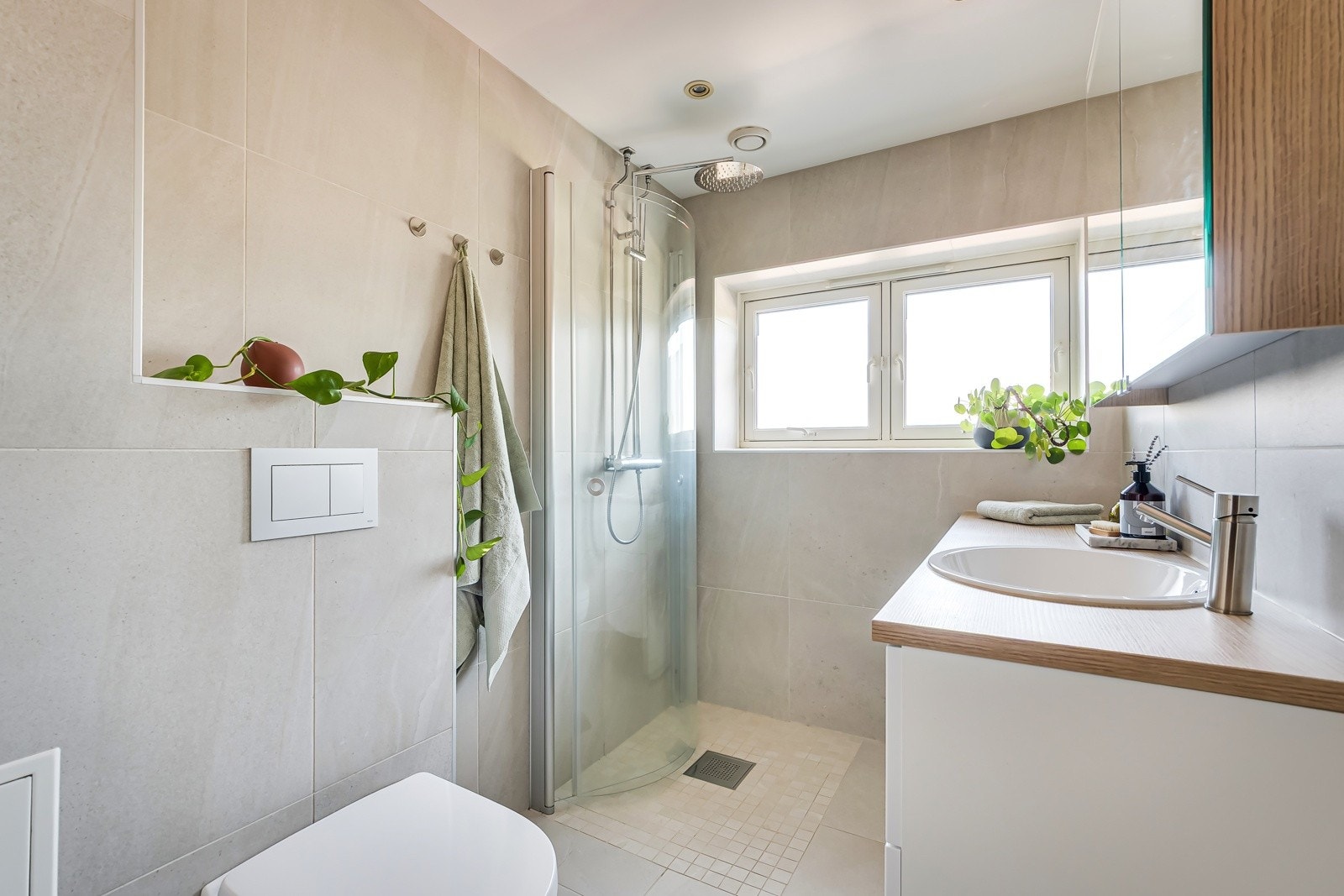 Et pent og tidløst uttrykk preger rommet, med store fliser i harmoniske toner på både gulv og vegger, som gir en rolig og tidløs atmosfære. Luksus med vinduer som slipper inn deilig dagslys og gir ekstra luftning. Galleribilde