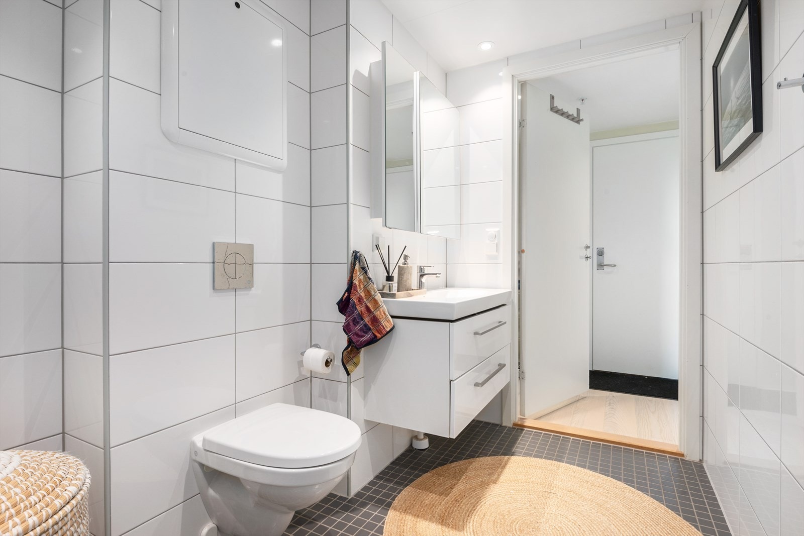 Badet er utstyrt med mekanisk avtrekk, opplegg for vaskemaskin, veggmontert wc, dusjhjørne med glassdører og ettgreps dusjbatteri i rustfritt stål. Galleribilde