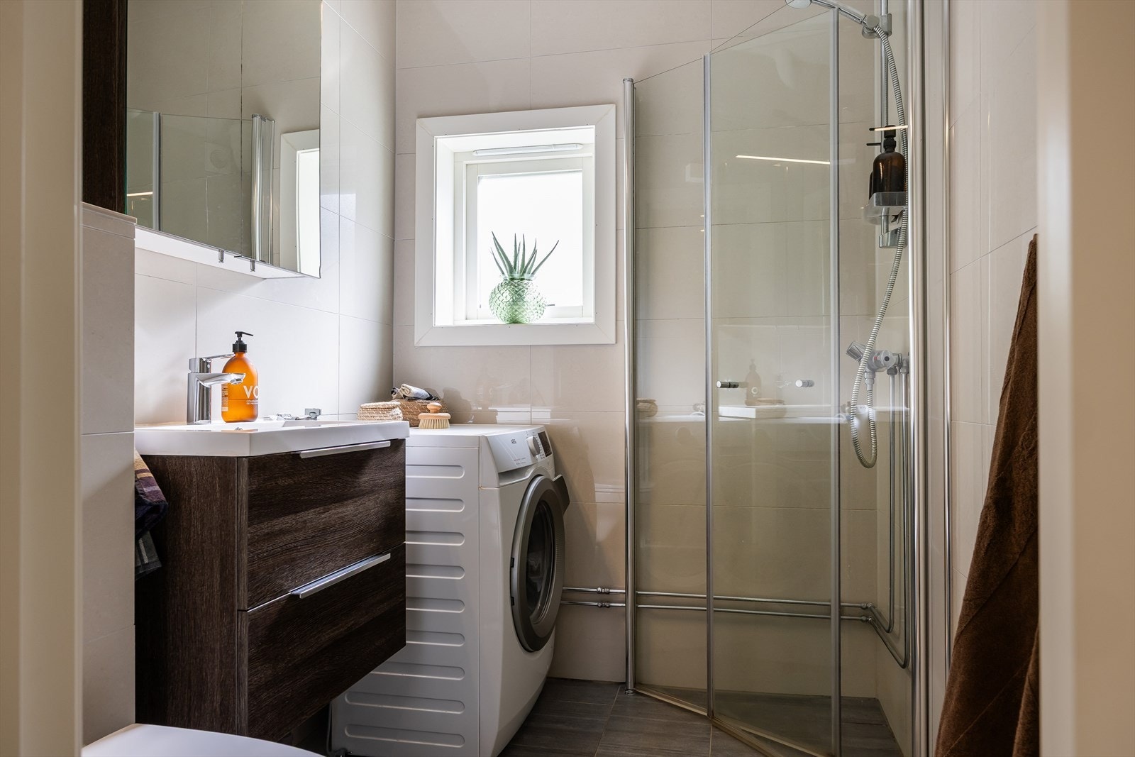Badet er innredet med nedfelt servant, veggmontert toalett, dusjvegger/hjørne og opplegg for vaskemaskin. Galleribilde