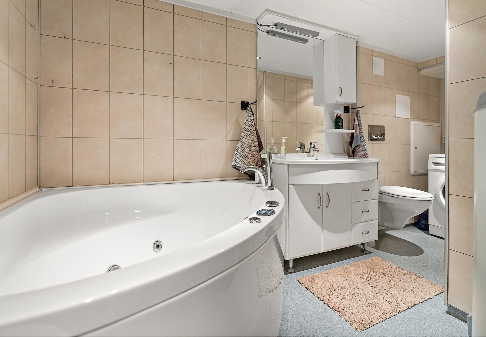 Badet i kjeller er innredet med nedfelt servant, veggfestet toalett, hjørnebadekar og opplegg for vaskemaskin. Galleribilde