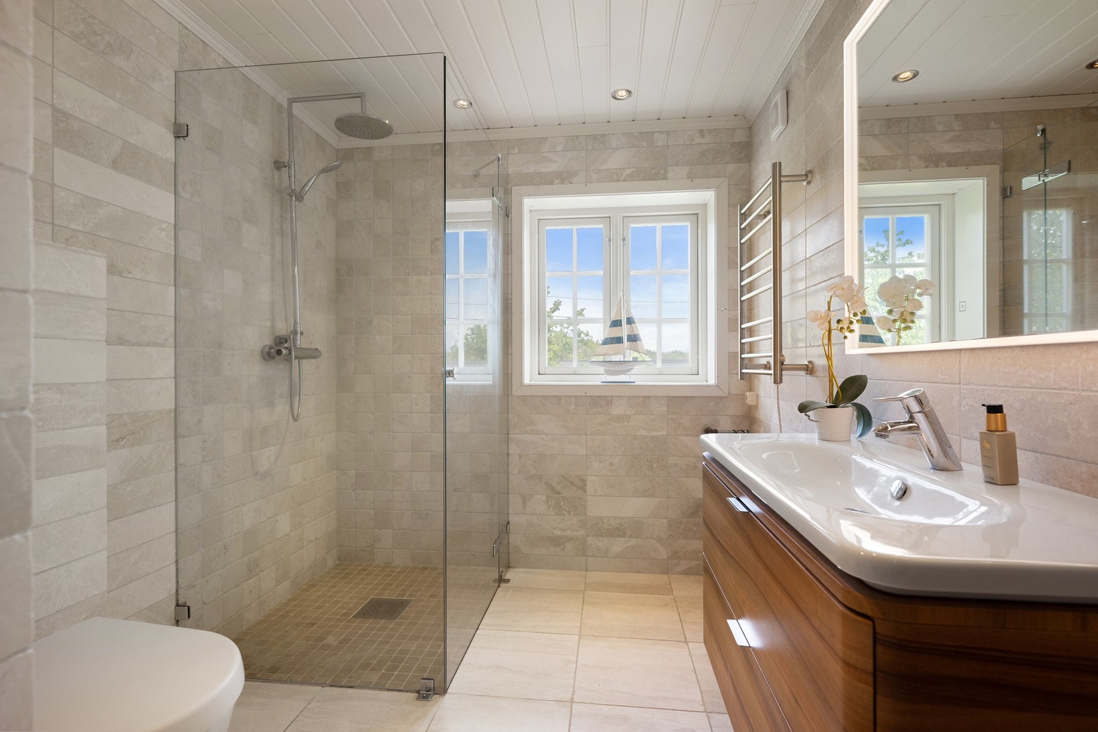 Badet i underetasjen er kombinert bad og vaskerom. Rommet er innredet med vegghengt toalett, dusjhjørne med glassvegger og baderomsinnredning med heltstøpt servant med skuffer under samt et vegghengt høyskap. Galleribilde