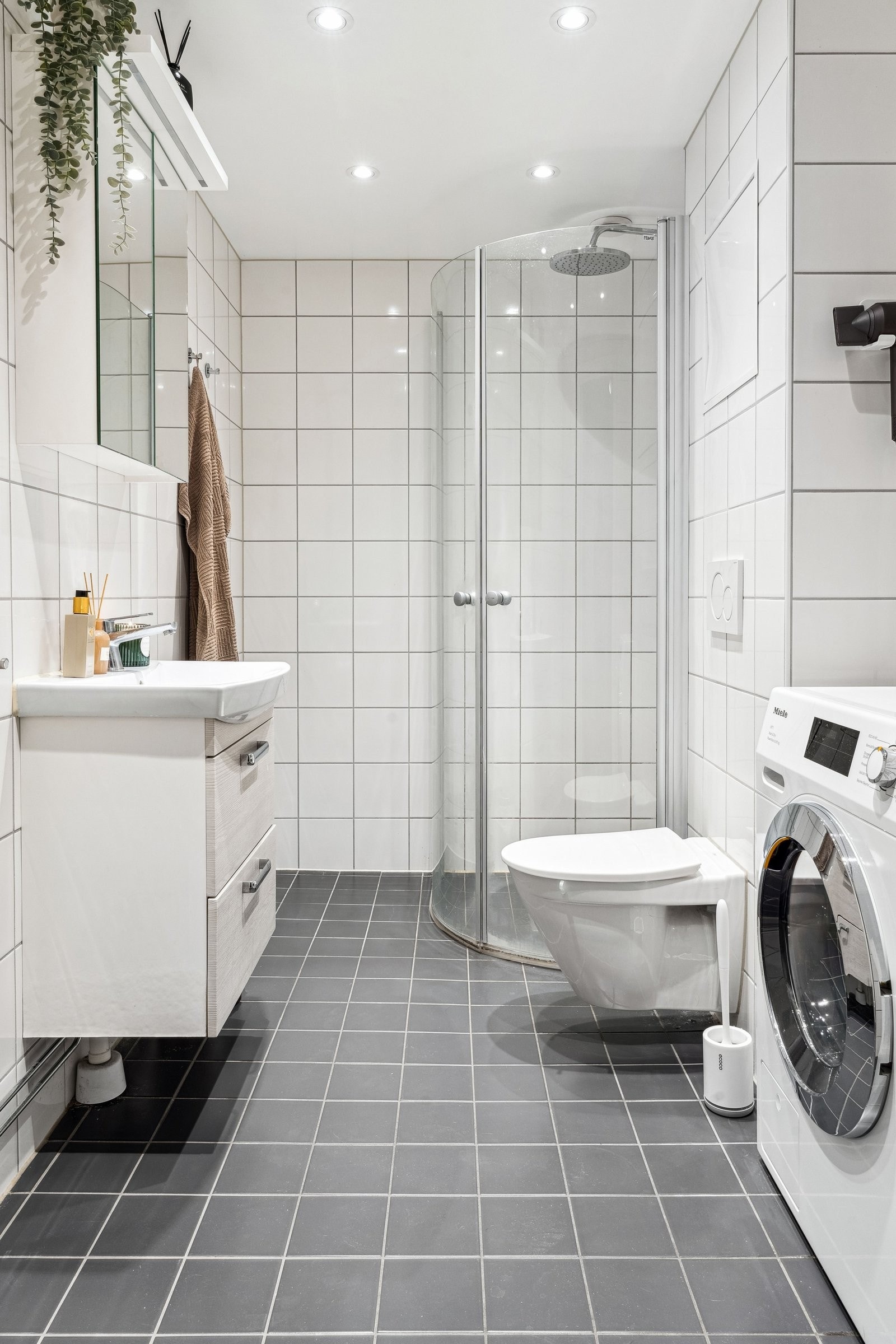 Baderomsinnredningen består av servantskap med helstøpt servant, speilskap, vegghengt toalett og dusjhjørne med buende svingdører av herdet glass, sluk av plastmateriale med klemring og synlig membran Galleribilde