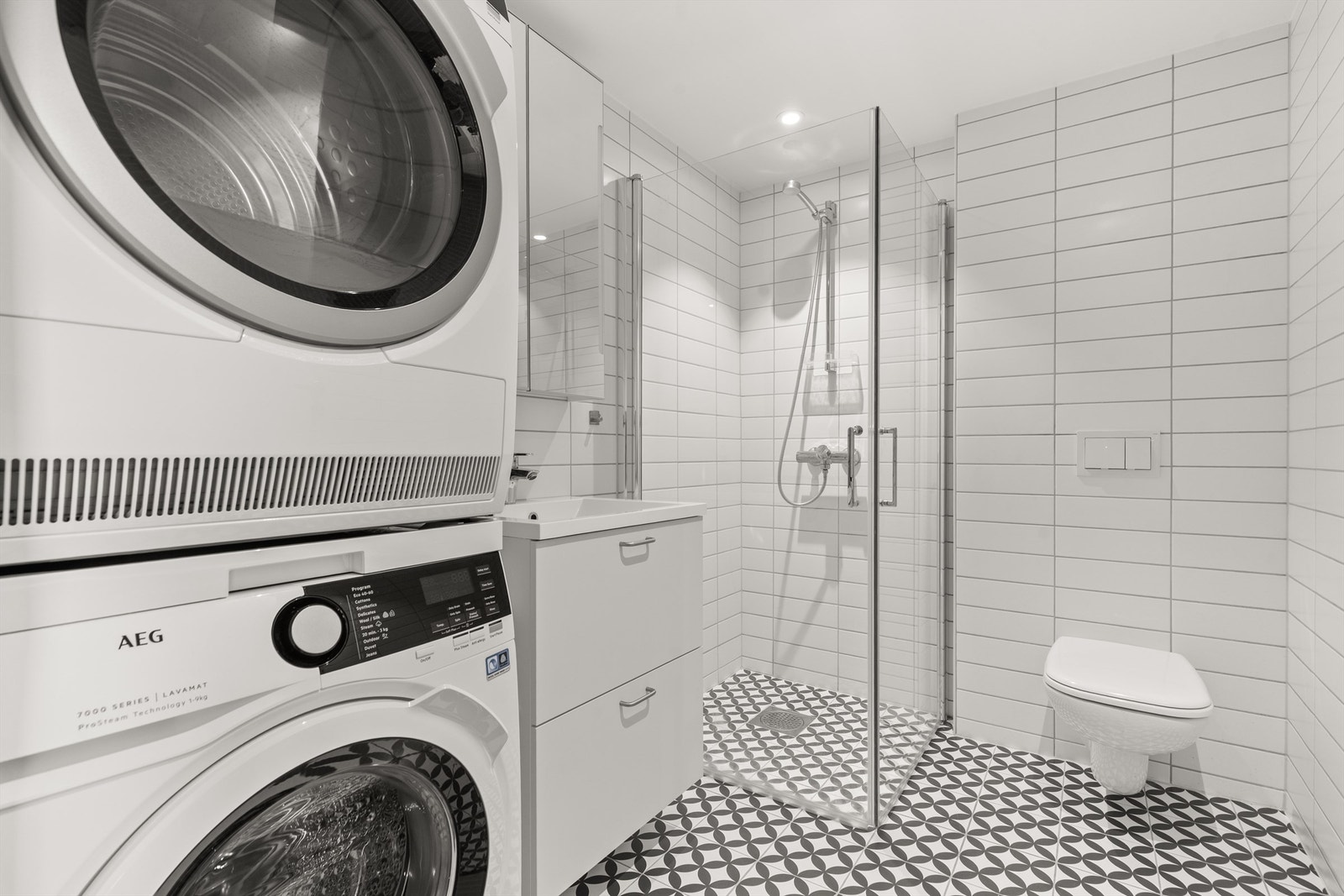 Delikat og flislagt bad med behagelig gulvvarme. Innredningen består av servantinnredning, speilskap og dusjhjørne med innfellbare glassdører. Galleribilde