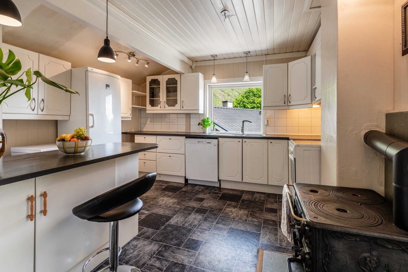 Et romslig og praktisk kjøkken med gode arbeidsflater, integrerte løsninger og koselig vedovn som gir både varme og stemning Galleribilde