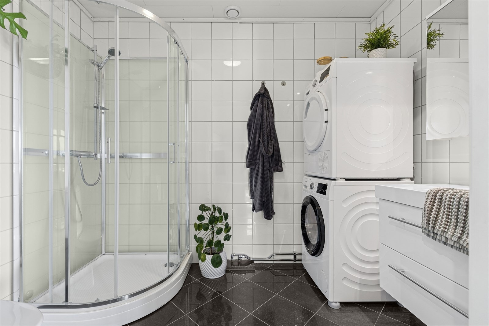 Helfliset baderom med dusjkabinett, hvit baderomsinnredning, toalett og opplegg for vaskemaskin. Galleribilde