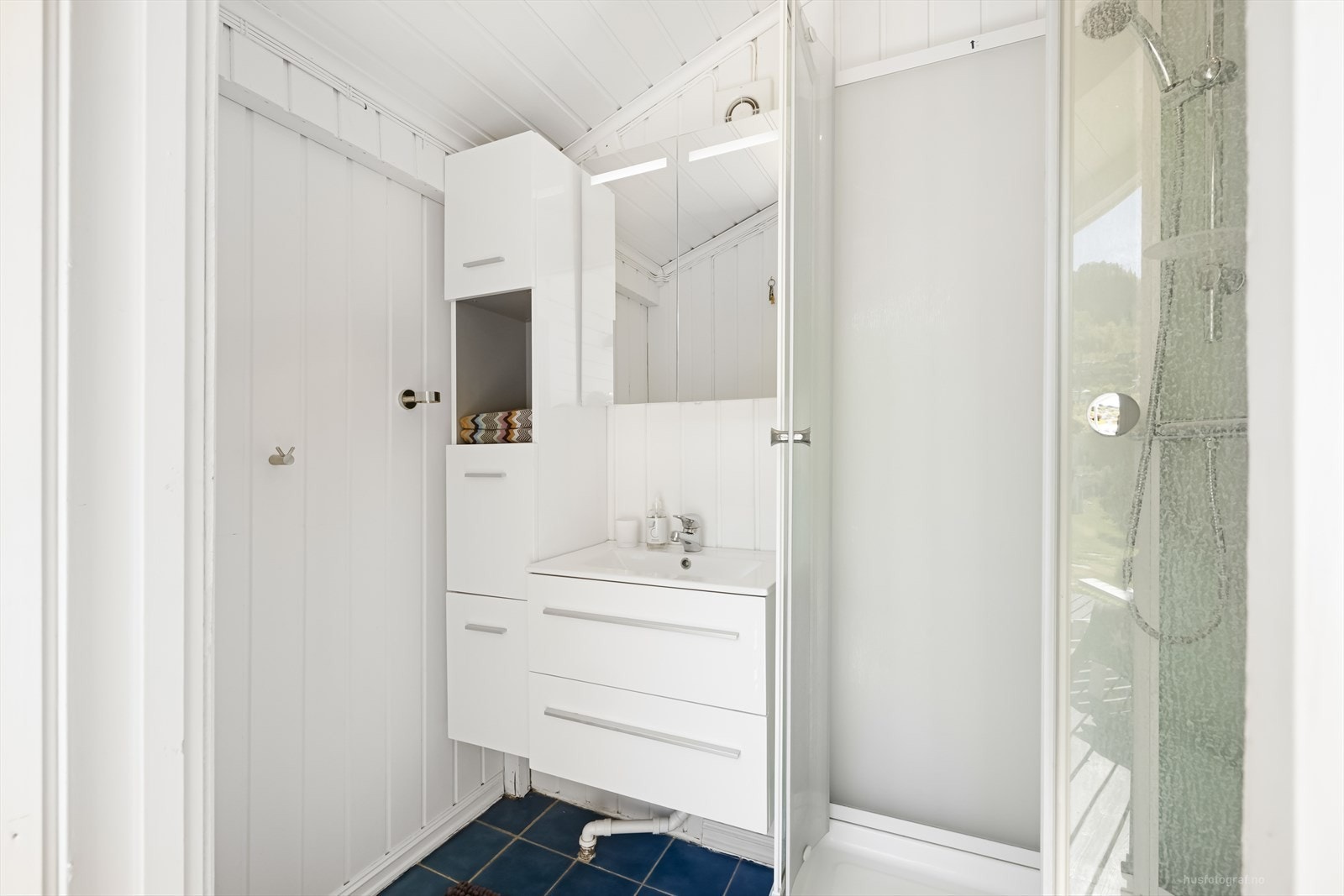 Innredet hygienerom/bad i hovedhuset, utstyrt med servant med skuffer, høyskap, speilskap med belysning og dusjkabinett. Galleribilde