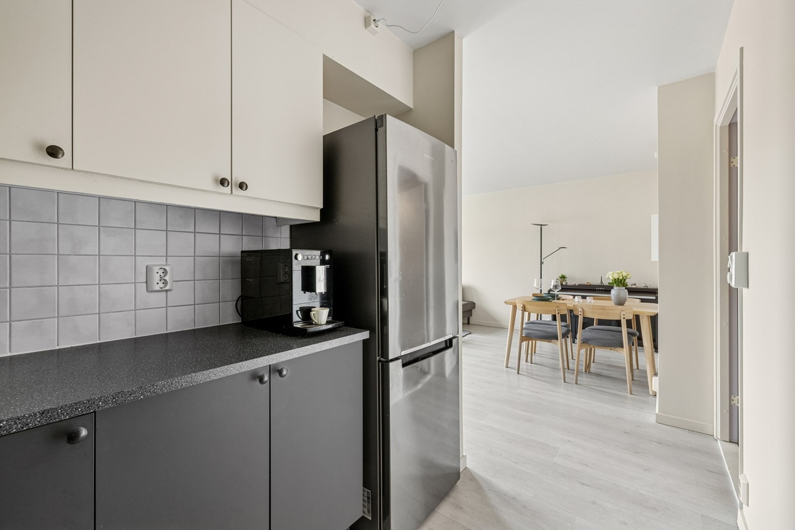 Kjøkkeninnredning med slette fronter, overskap med benkebelysning og fliser på vegger. Mørk laminat benkeplate med nedfelt stålkum og ett-greps armatur. Integrert avtrekksvifte i overskap. Opplegg for
komfyr, oppvaskmaskin og kjøl/frys. Galleribilde