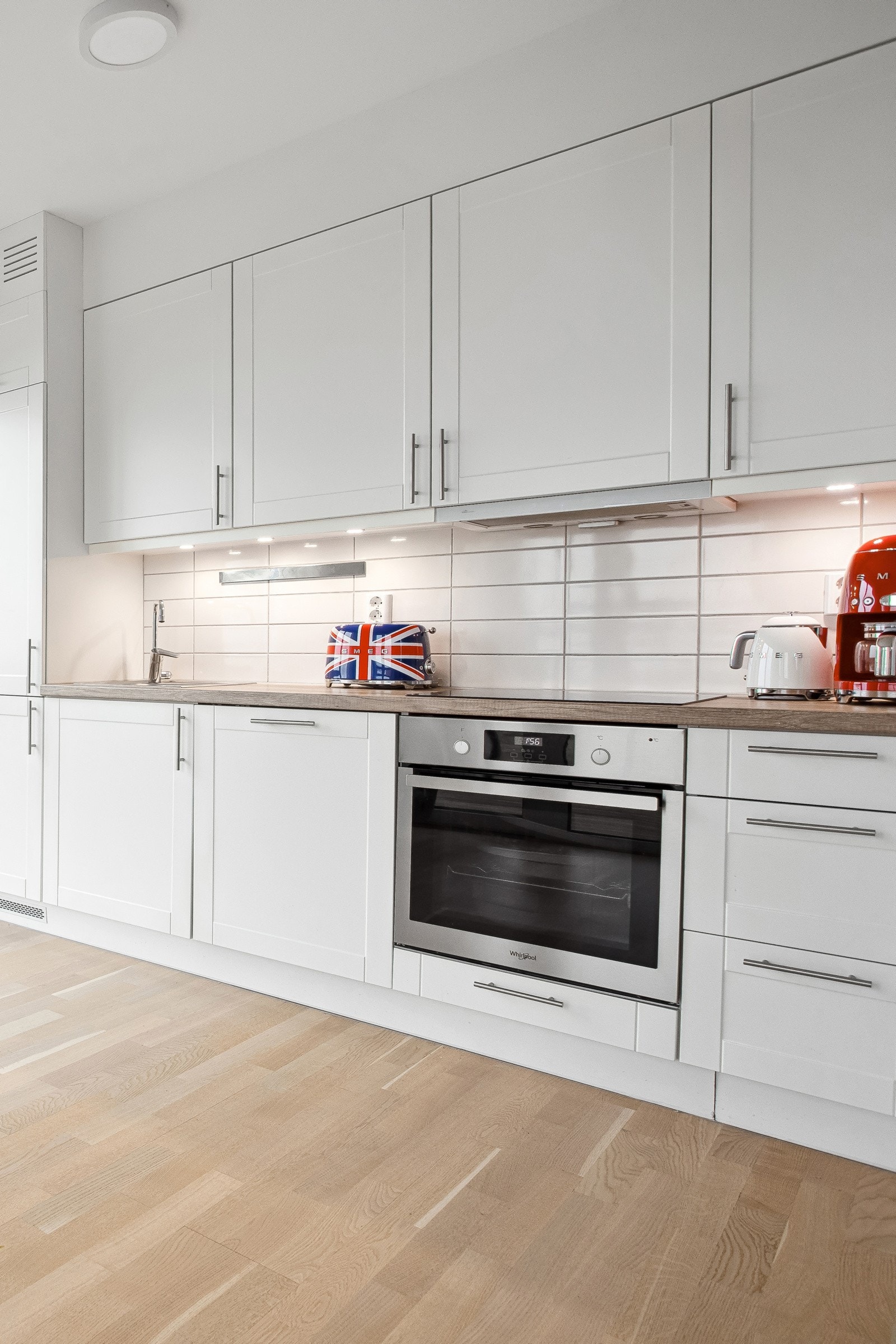 Det er fliser mellom benkeplate og overskap. Lys under overskap. Galleribilde