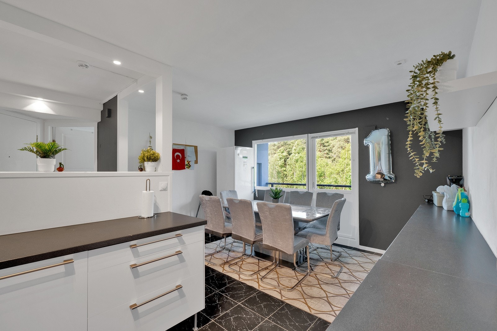 Spiseplassen er plassert ved store vindusflater som gir rikelig med naturlig lys og utgang til balkong. Langs veggen er det montert lavt vitrineskap med frostede glassdører for praktisk oppbevaring. Galleribilde