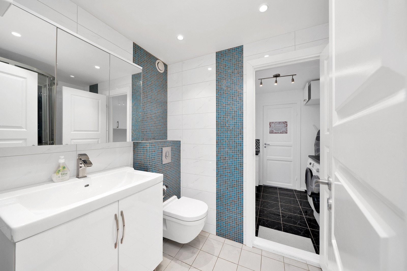 Høyglans baderomsinnredning med glatte fronter og en helstøpt servant med integrert vask. Servanten er utstyrt med ettgreps blandebatteri i kromutførelse. I hjørnet av rommet er det plassert et buet dusjkabinett med herdet glass og tilhørende dusjarmatur. Galleribilde