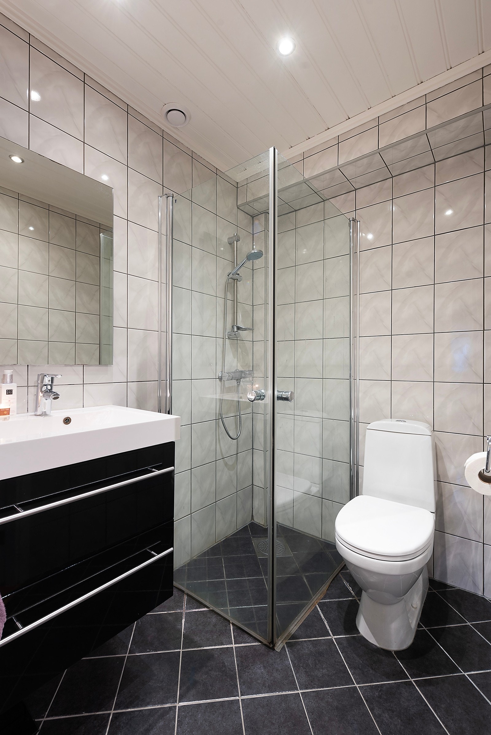 Badet er flislagt med mørke fliser på gulv og hvite fliser på veggene Galleribilde