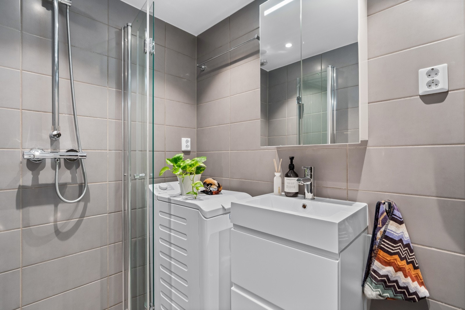 Badet består av vegghengt toalett, servant og servantskap, dusjhjørne med to foldbare glassdører og opplegg for vaskemaskin. Naturlig ventilasjon. Galleribilde