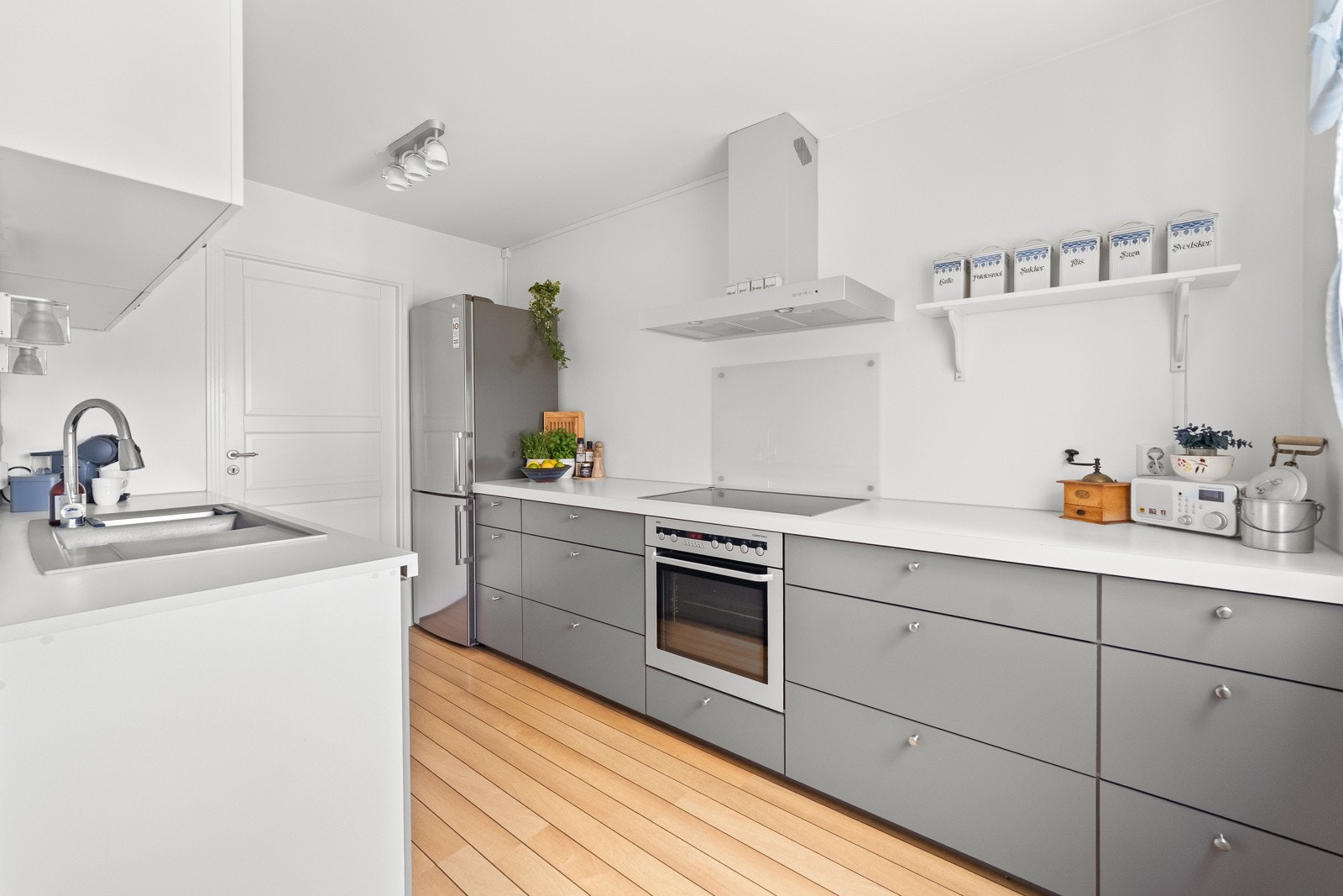 Kjøkkenet har innredning med grå, glatte fronter. Benkeplaten er av laminat. På kjøkkenet er det integrert oppvaskmaskin, platetopp og stekeovn samt kjøkkenventilator med kullfilter Galleribilde