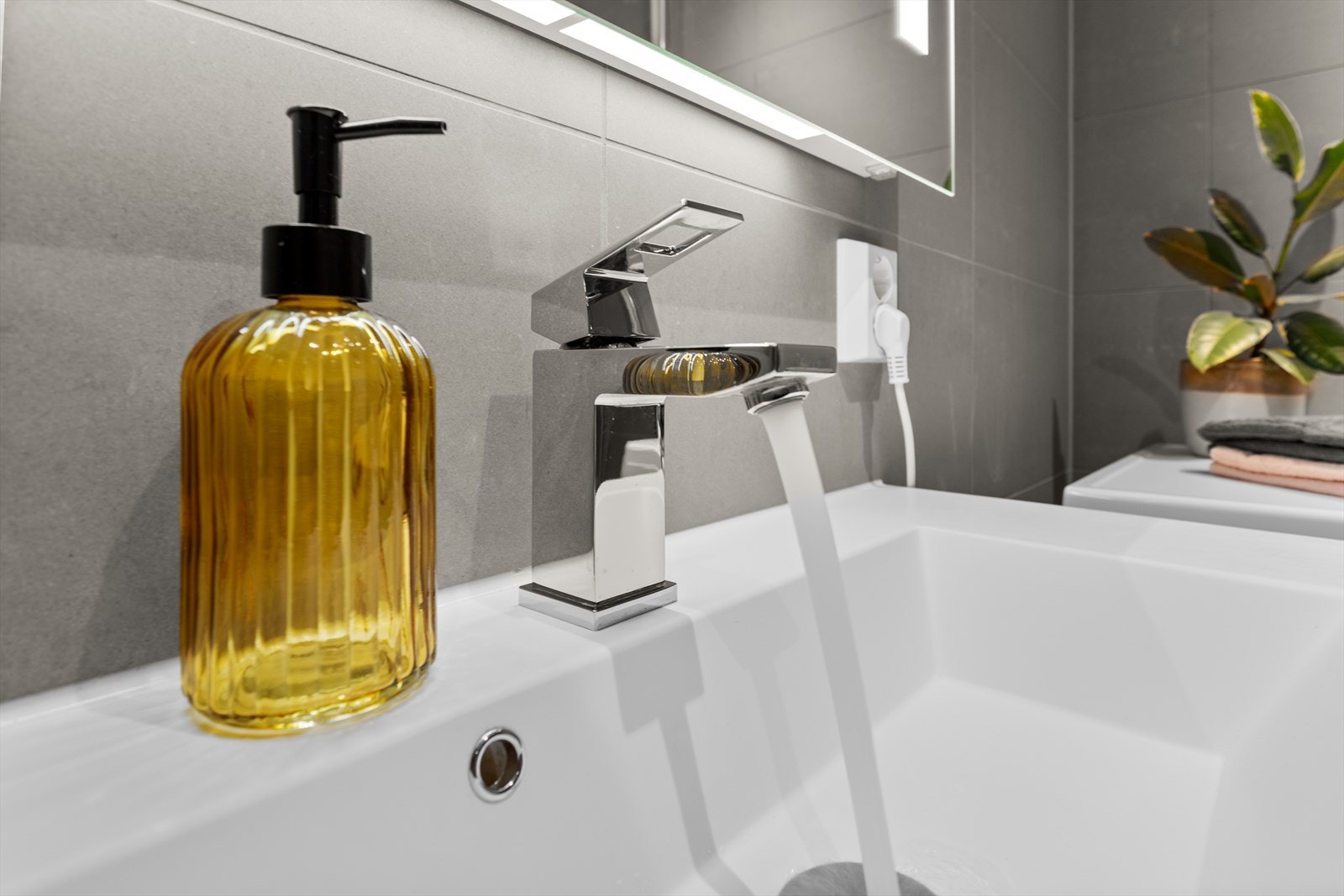 Badet er innredet med heldekkende servant på underskap, speil med belysning, vegghengt toalett og dusjhjørne med dusjvegger i herdet glass. Galleribilde