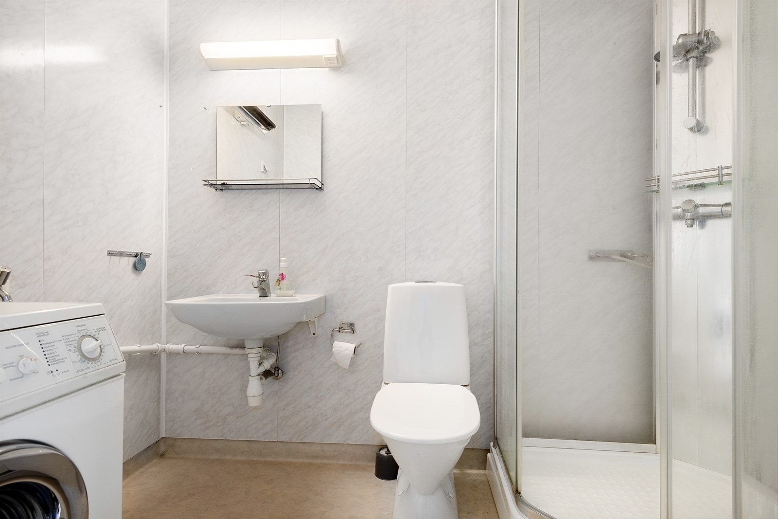 Bad leilighet 1. Dusjkabinett, gulvmontert toalett, servant med
ett-greps blandebatteri og opplegg for vaskemaskin. Bør renoveres grunnet alder. Galleribilde