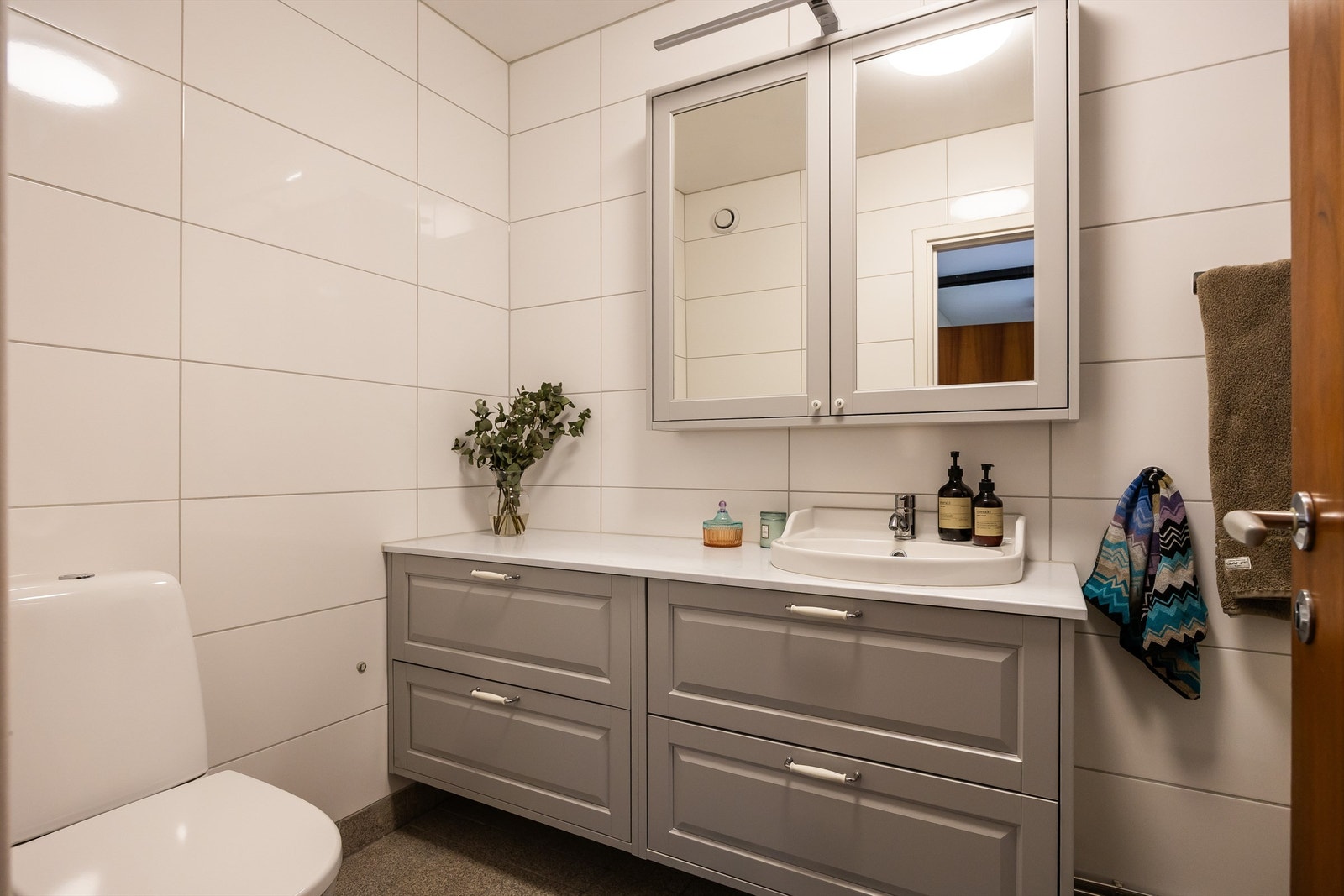 Baderommet er innredet med vegghengt servantskap med romslige skuffer og benkeplate med ovenpåliggende servant, speilskap med stikkontakter og overbelysning, dusjkabinett og frittstående toalett. Galleribilde