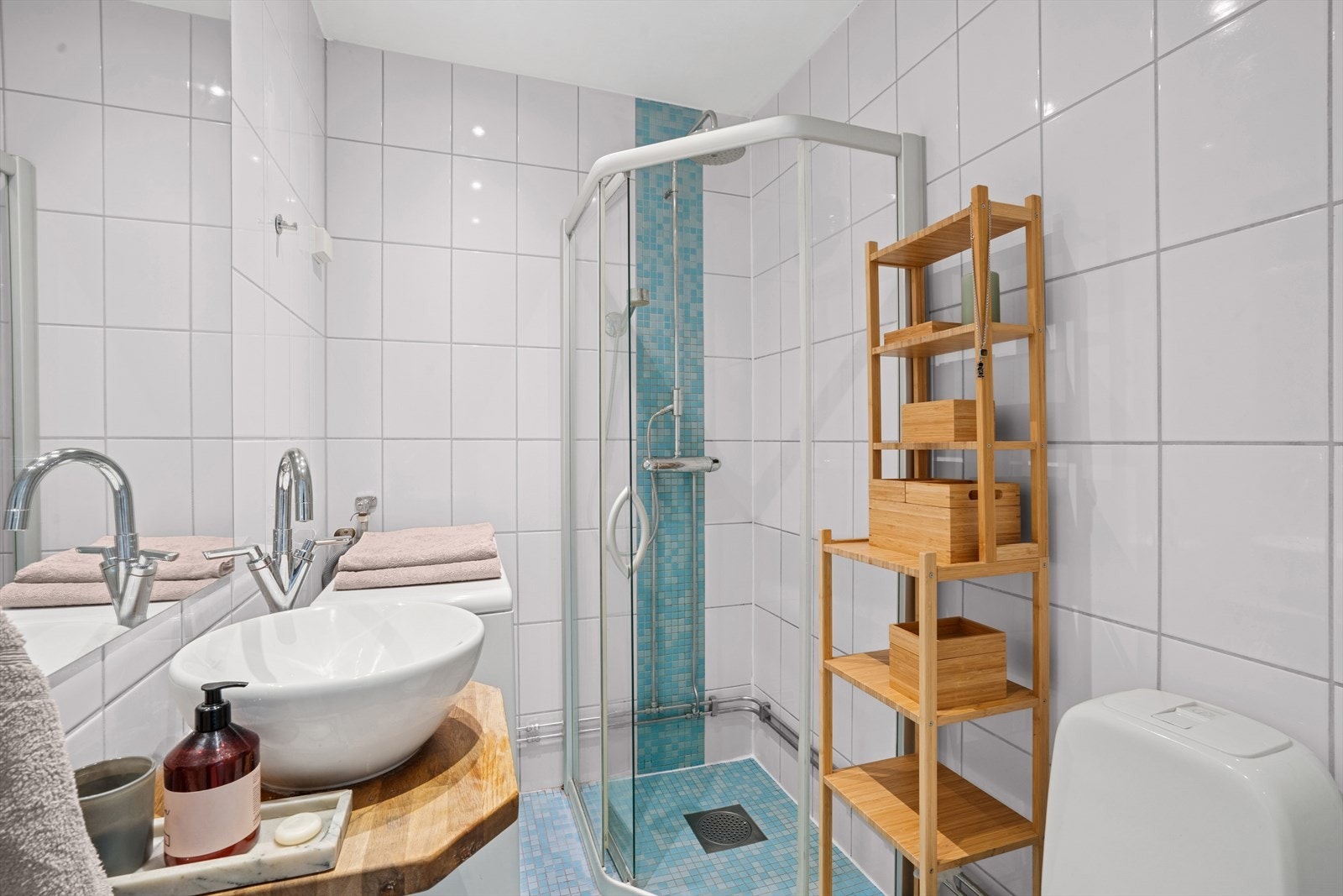 Badet er innredet med dusjkabinett, vegghengt servant, vaskemaskin og praktisk oppbevaringshylle i tre. Galleribilde
