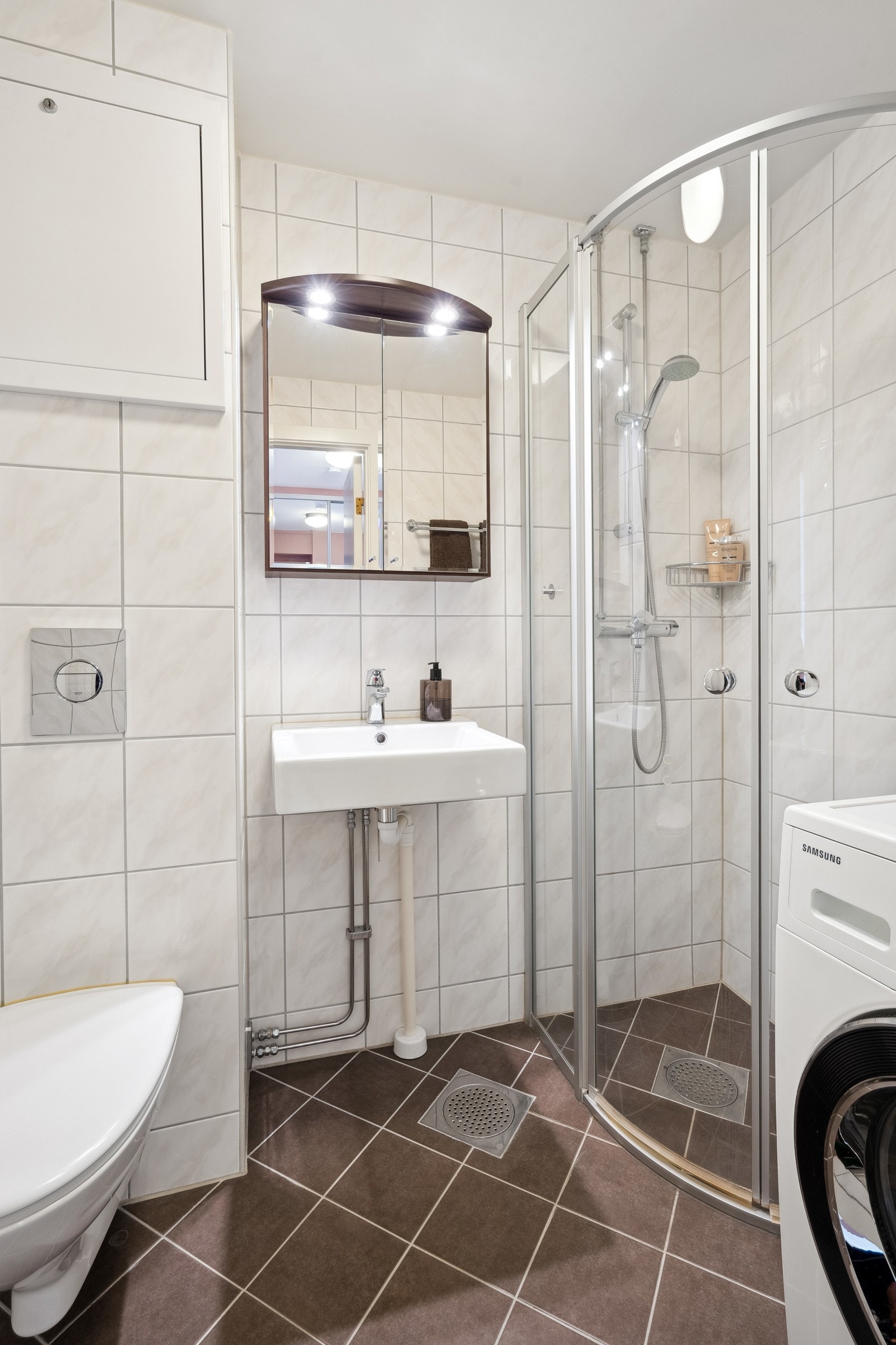 Badet er innredet med servant, veggspeil, veggmontert toalett og dusjhjørne Galleribilde