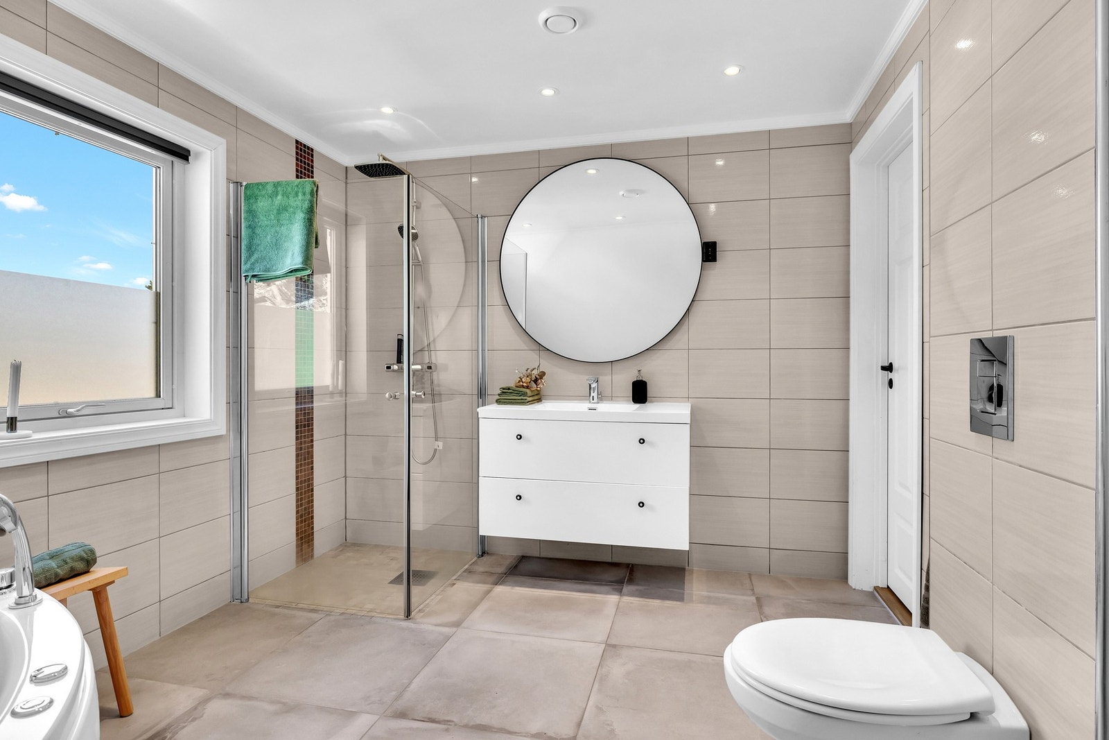 Baderommet inneholder vegghengt servantskap, dusj med glassdører, vegghengt toalett og boblebad. Galleribilde