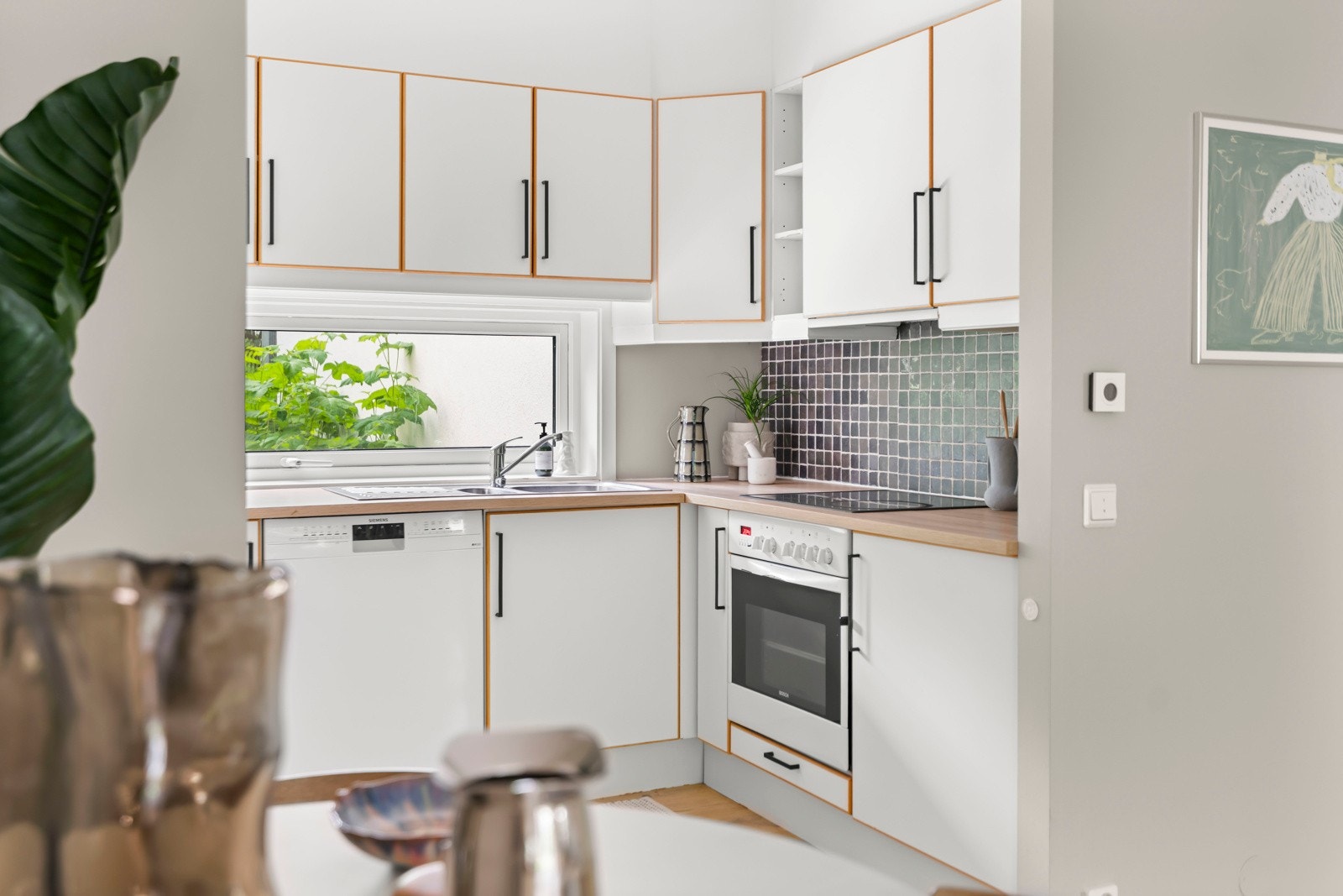 Et lyst og innbydende kjøkken med praktisk utforming. Innredningen er fra byggeår og byr på glatte, folierte fronter som gir et tidløst uttrykk. Galleribilde