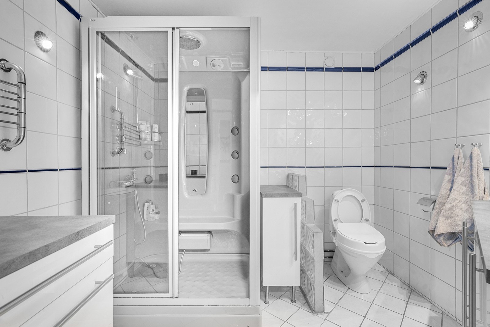 Badet fremstår som funksjonelt og praktisk innredet, med flislagte gulv og vegger som gir et rent og tidløst uttrykk. Gulvet har elektriske varmekabler som gir behagelig varme, og himlingen er malt i en lys og nøytral tone Galleribilde