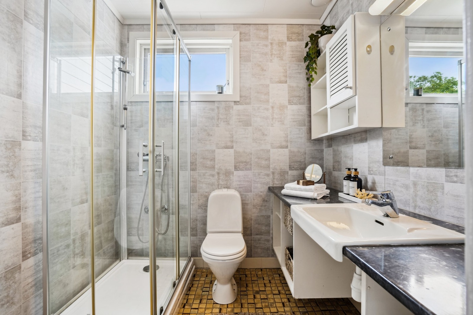 Badet har dusjkabinett, toalett og servantinnredning. Det er fliset gulv og tapet på veggene. Galleribilde