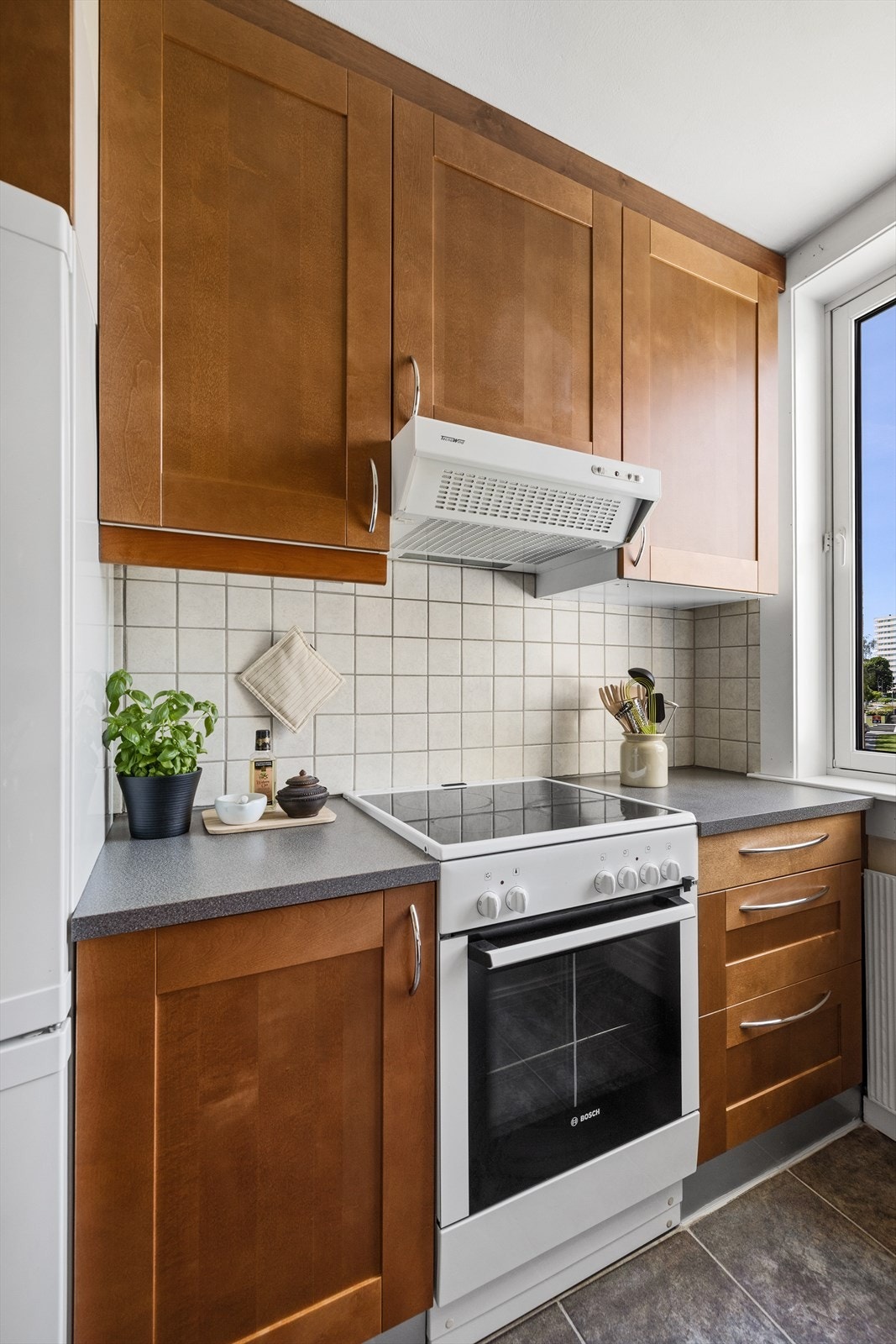 Kjøkkeninnredning fra IKEA med profilerte fronter i mørkbeiset tre, en grå benkeplate med nedfelt vask i rustfritt stål og kromfarget blandebatteri. Galleribilde