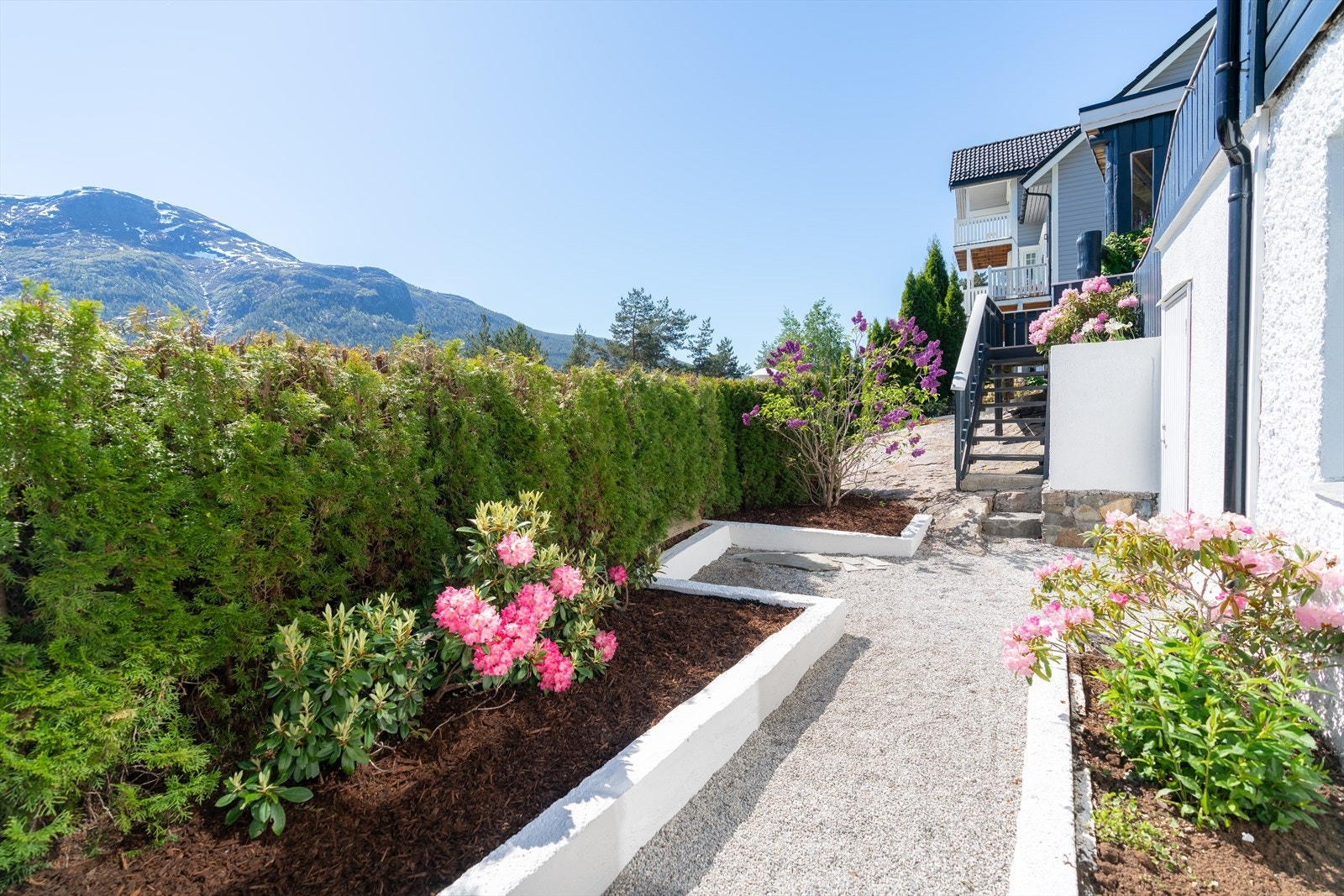 Frå terrassen har ein tilkomst til hage med hekk, blomsterbedd og grusa gangbaner. Galleribilde